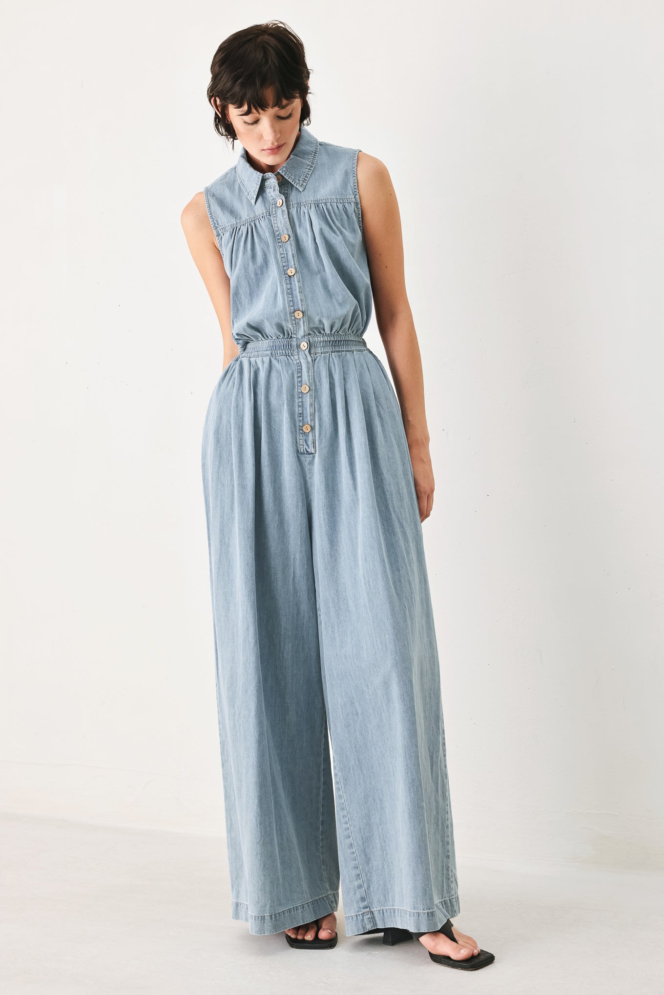 Woman wearing a light blue denim jumpsuit featuring collar, front button down, sleeveless, wide leg, elastic back waistband and popover | FREEMARKET