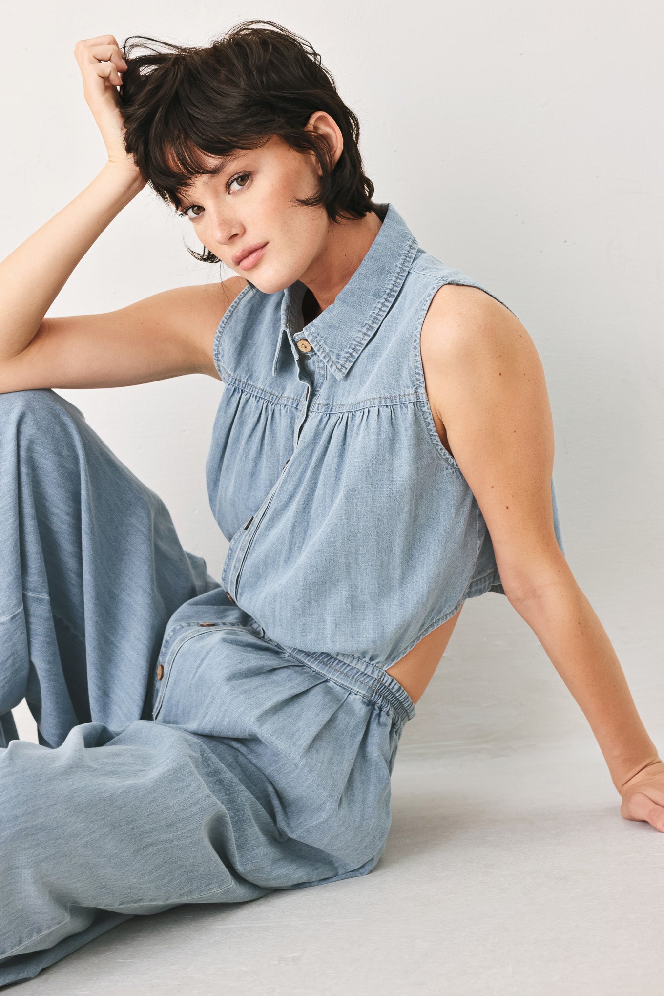 Woman wearing a light blue denim jumpsuit featuring collar, front button down, sleeveless, wide leg, elastic back waistband and popover | FREEMARKET