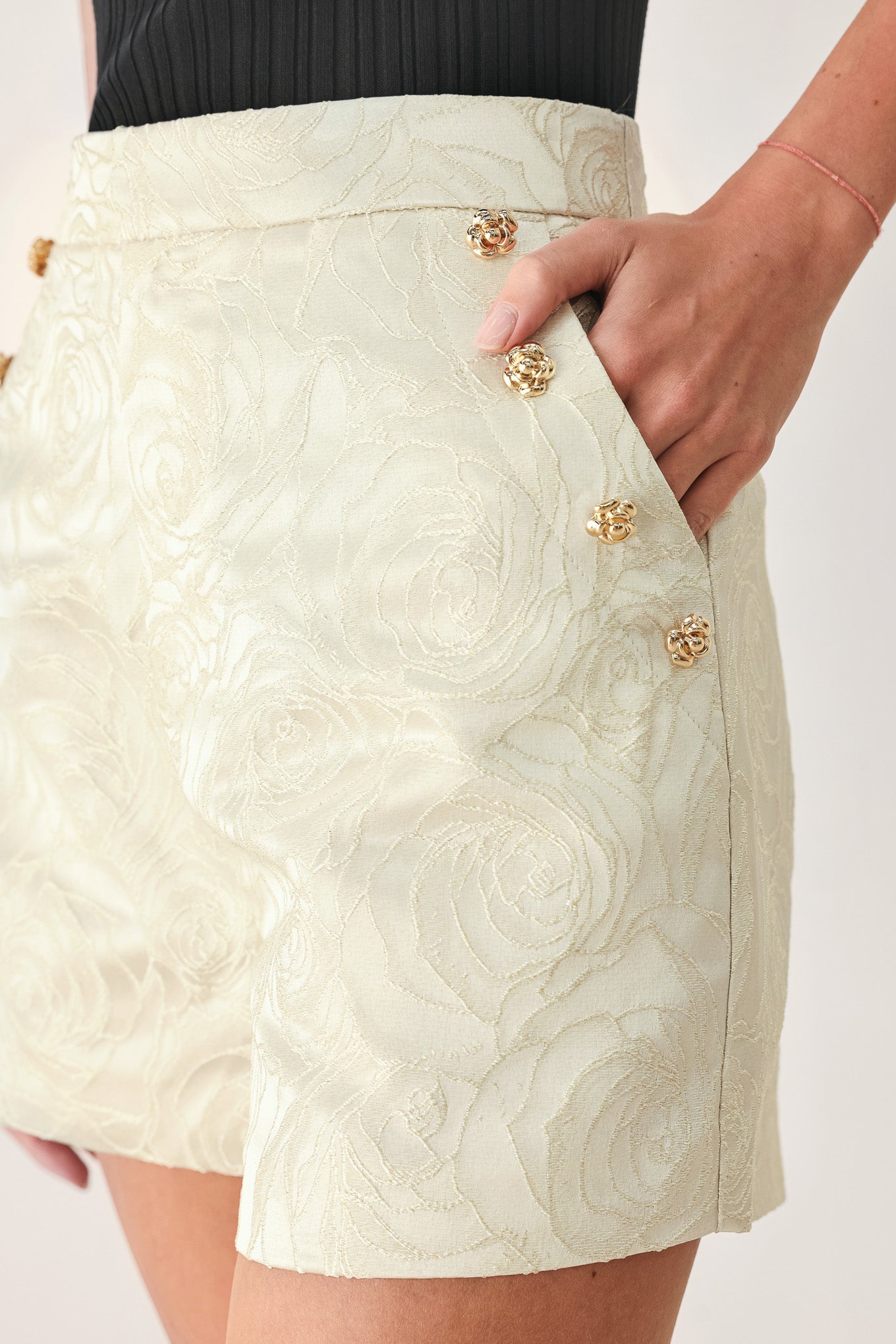 Woman wearing high-waisted cream shorts with a subtle embossed swirl pattern and decorative gold-tone buttons down the side pocket | FREEMARKET