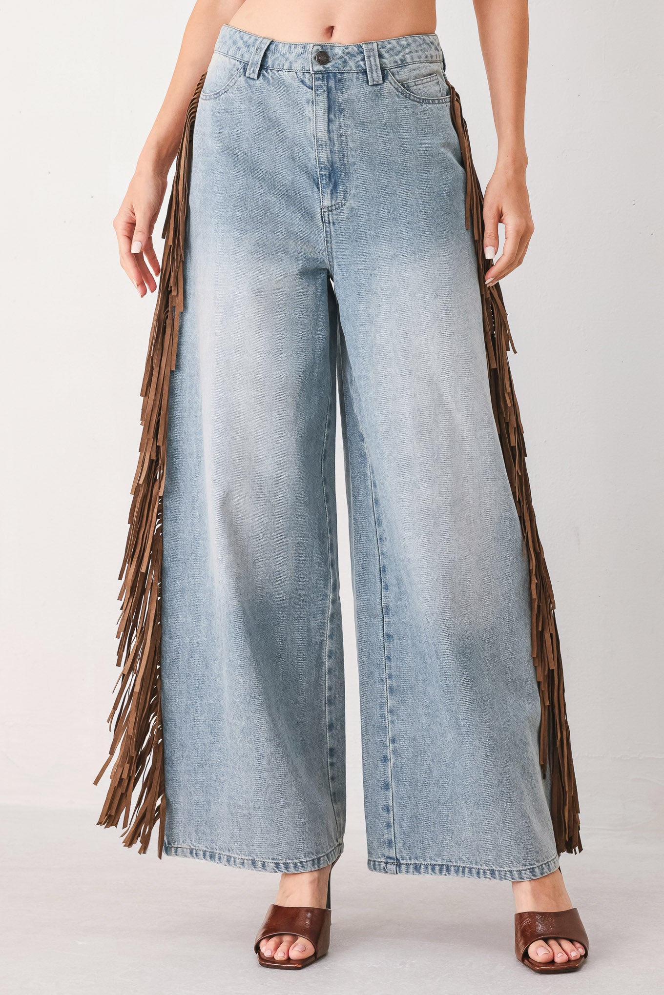 A model wearing light-wash blue wide-leg denim jeans with long brown fringe detailing running down the outer sides | FREEMARKET