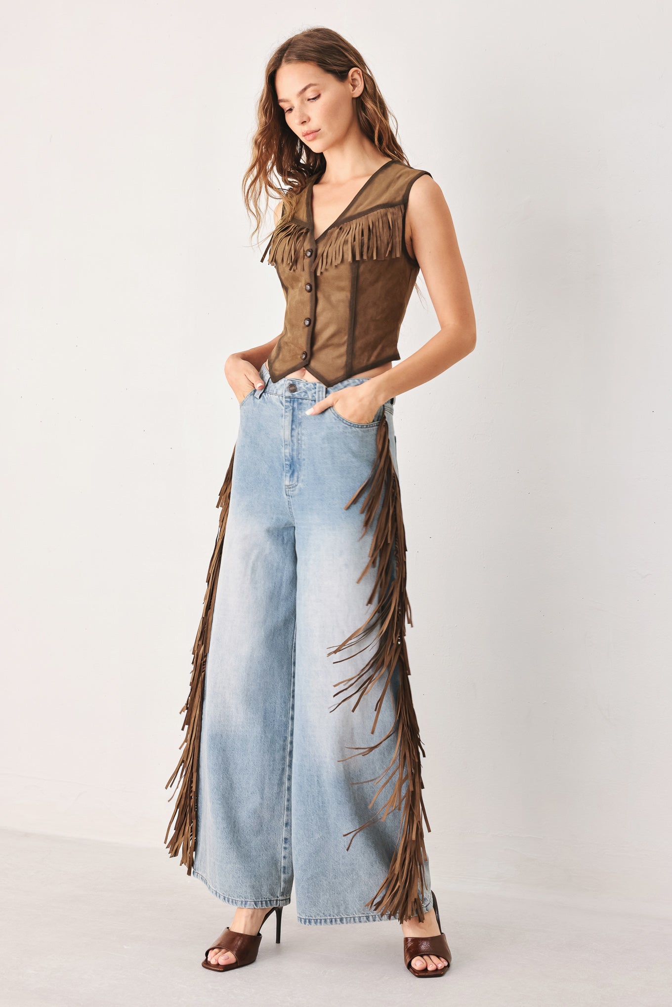 A model wearing light-wash blue wide-leg denim jeans with long brown fringe detailing running down the outer sides | FREEMARKET