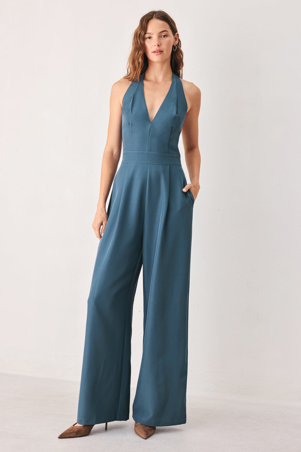 A woman modeling a teal blue halter-neck wide-leg jumpsuit with a deep V-neckline and side pockets | FREEMARKET
