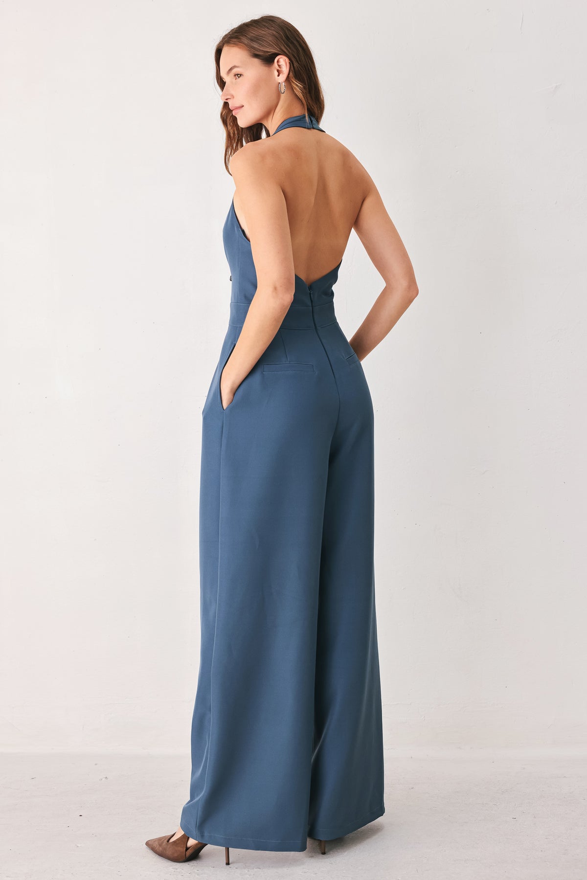 A woman modeling a teal blue halter-neck wide-leg jumpsuit with a deep V-neckline and side pockets | FREEMARKET