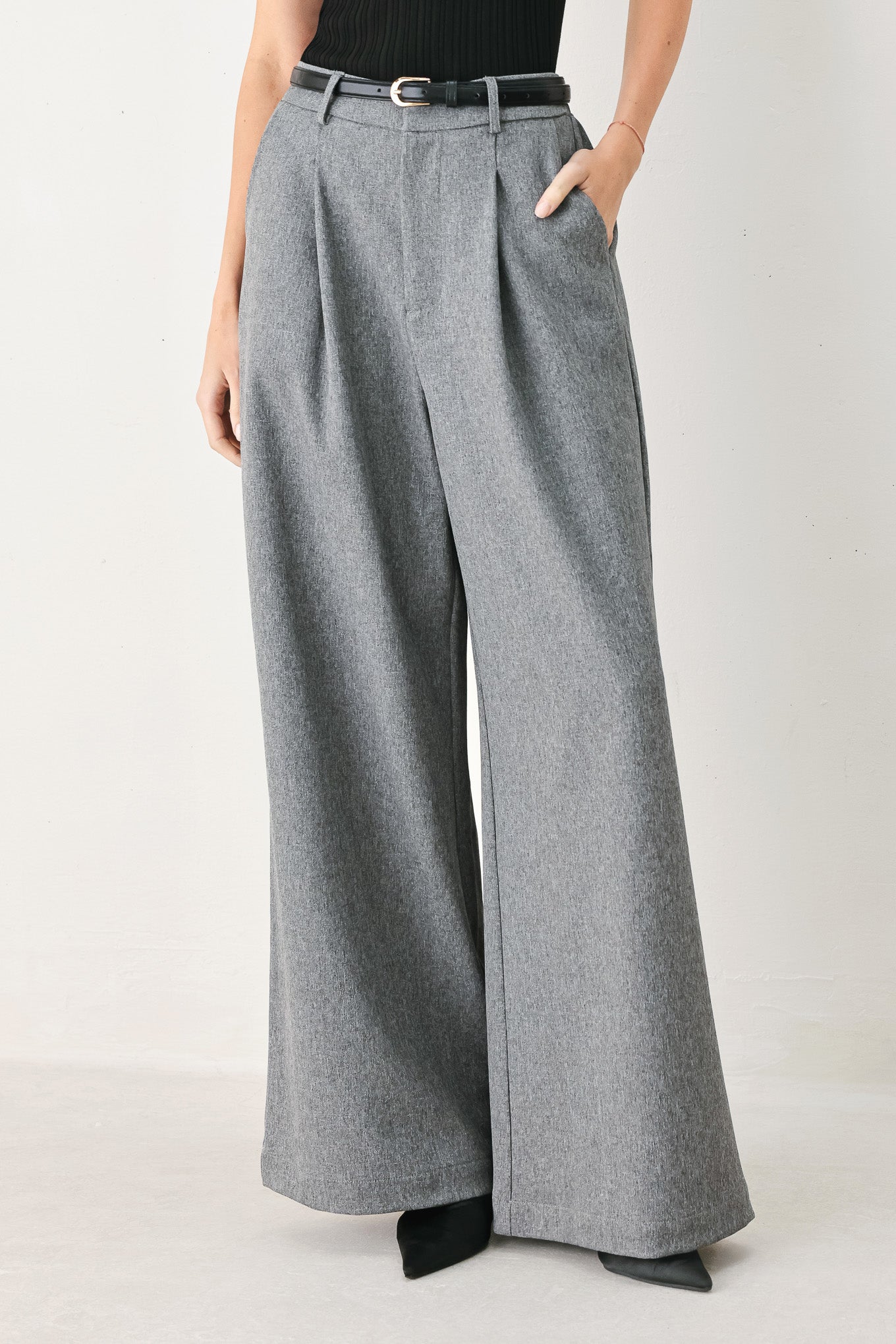 Woman wearing gray wide-leg pant with front closure, single pleat, pockets, and black belt | FREEMARKET