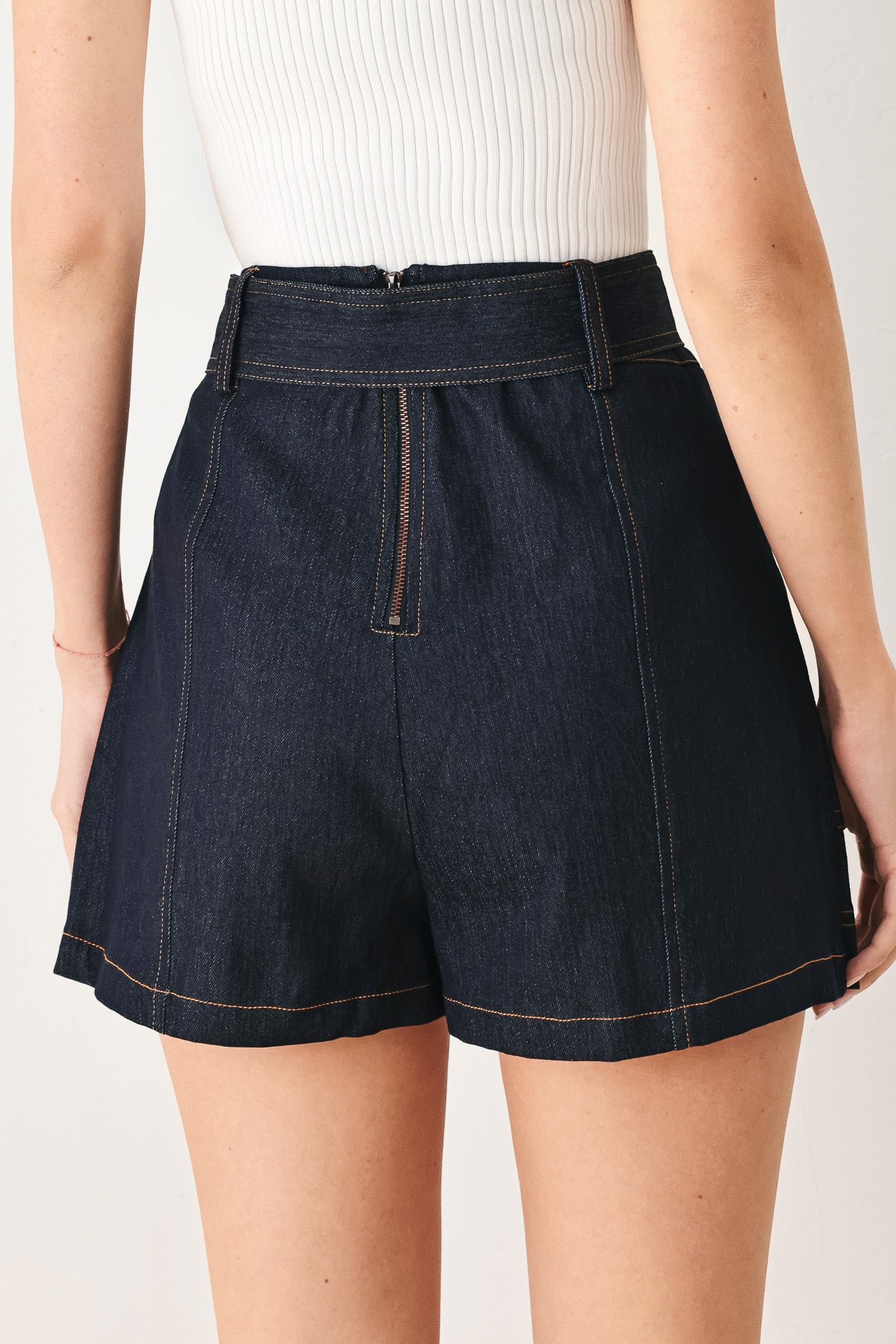 Woman wearing a dark denim skort with belt, front button detail and back zipper closure | FREEMARKET