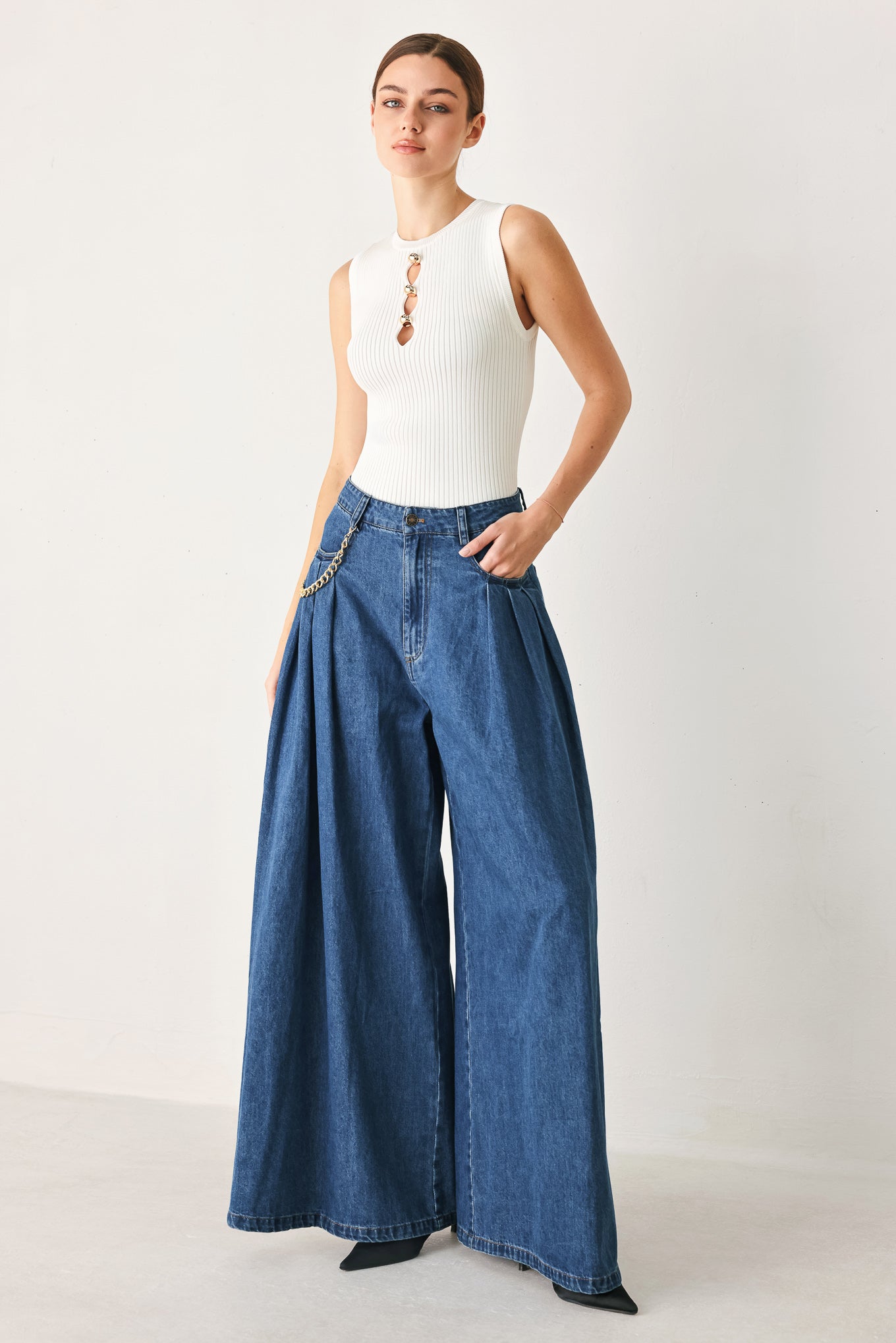 Woman wearing a pair of extra wide-leg blue denim jeans with front closure, pockets, pleats, and chain detail | FREEMARKET