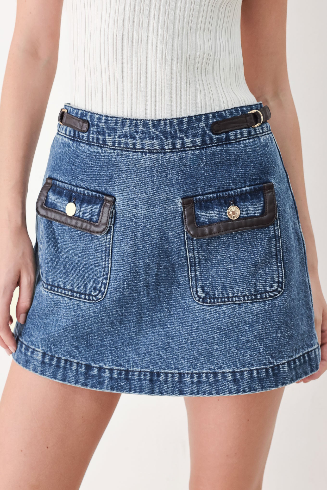 A model wearing a blue denim mini skort with dark brown leather accents on the waistband and pocket flaps | FREEMARKET