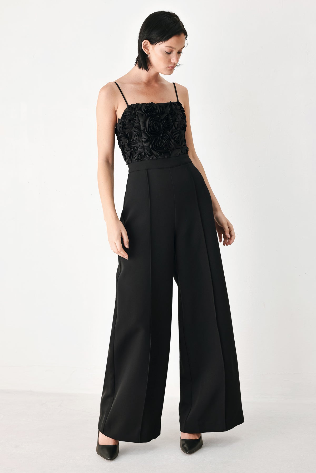A woman modeling a black sleeveless jumpsuit with a textured floral bodice and wide-leg trousers | FREEMARKET