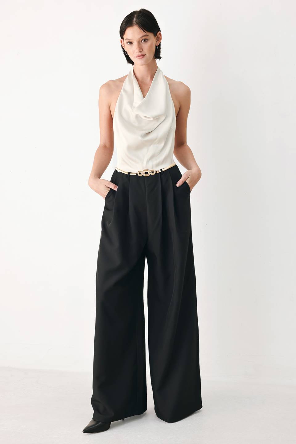 A model wearing a sleeveless jumpsuit with draped white top and black wide-leg trousers, and a thin gold belt with a round buckle | FREEMARKET