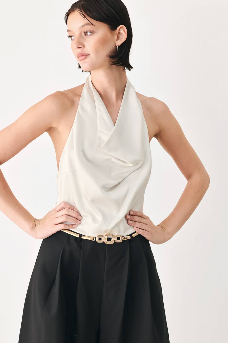 A model wearing a sleeveless jumpsuit with draped white top and black wide-leg trousers, and a thin gold belt with a round buckle | FREEMARKET