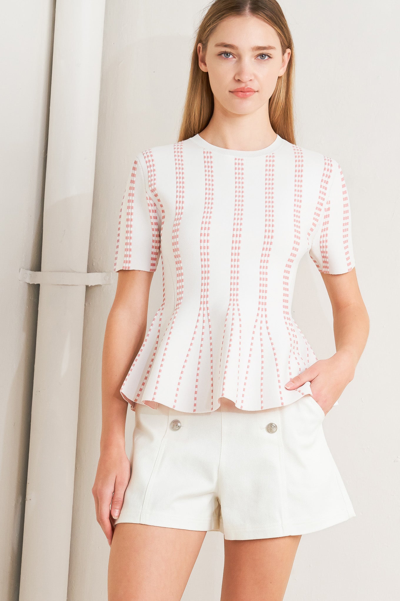 Woman wearing a pink blouse with white stitching against a neutral background AND A jacquard sweater top featuring round neckline, short sleeve and peplum FLYING TOMATO