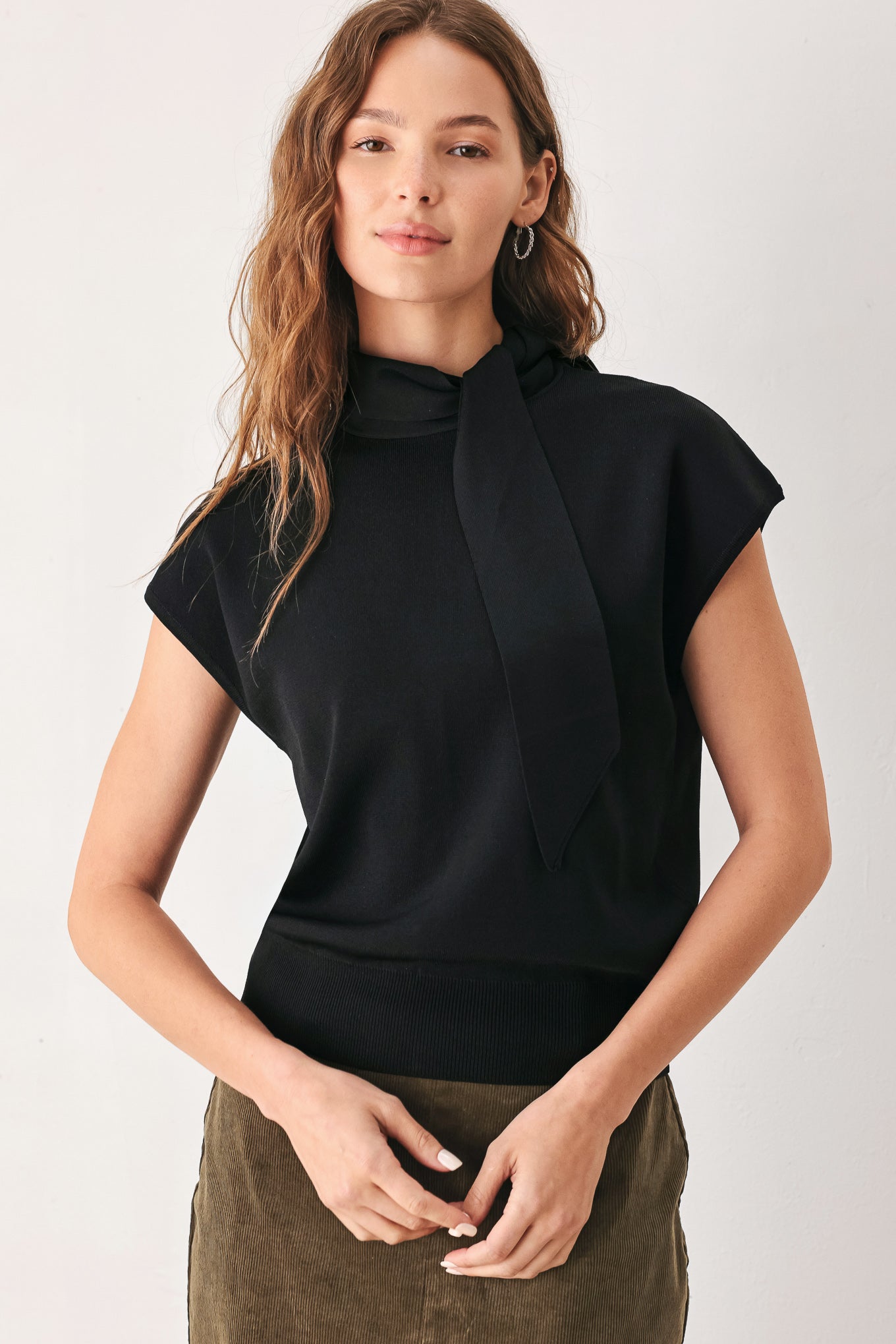 A woman wearing a black short-sleeve knit top with a high mock neck and a large draped tie detail at the front | FREEMARKET