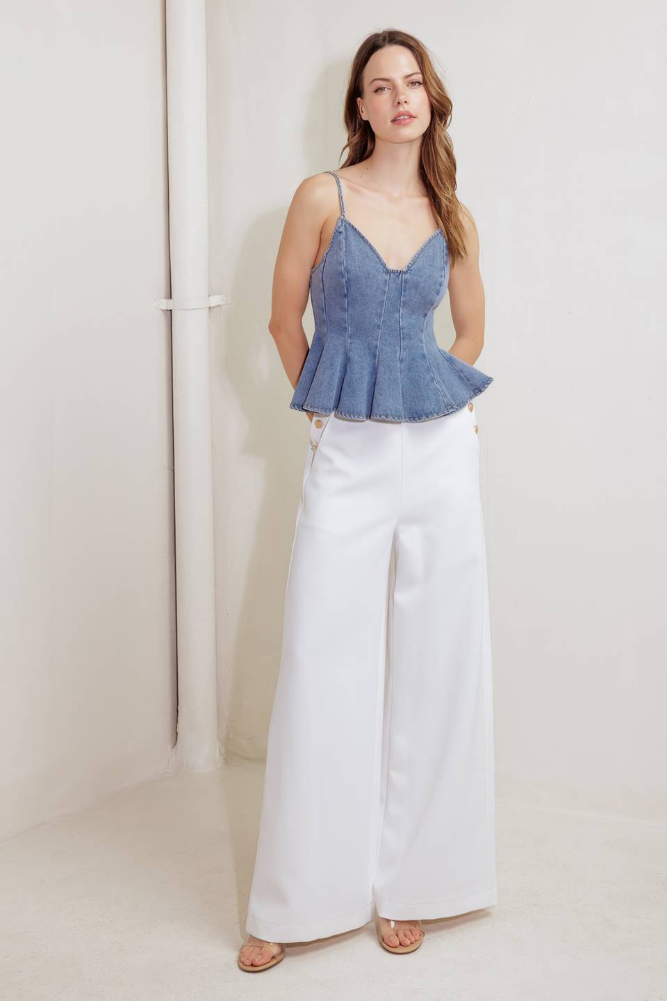 A washed denim cami top featuring straps, peplum and back zipper closure.