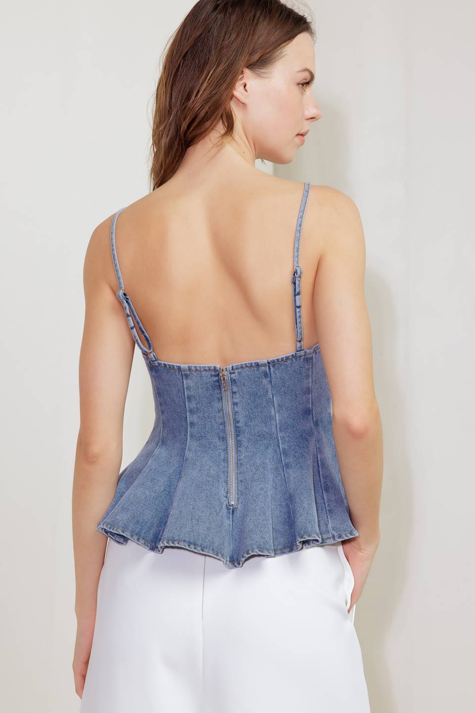 A washed denim cami top featuring straps, peplum and back zipper closure.