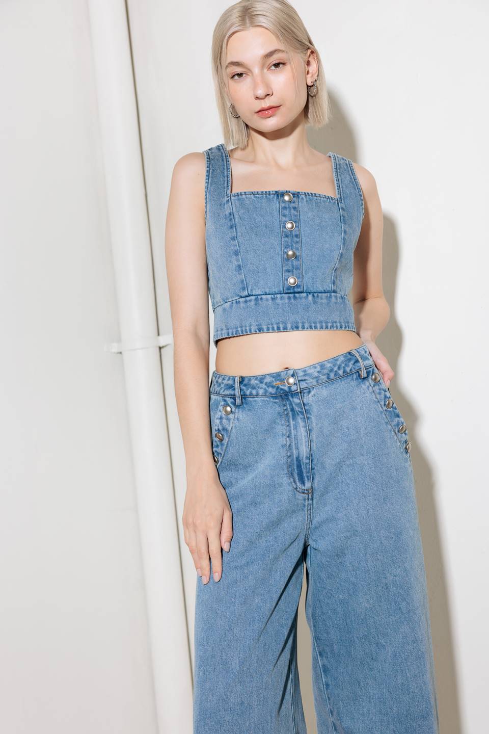 A washed denim top featuring square neckline, sleeveless, front button detail and smocked back with zipper closure.