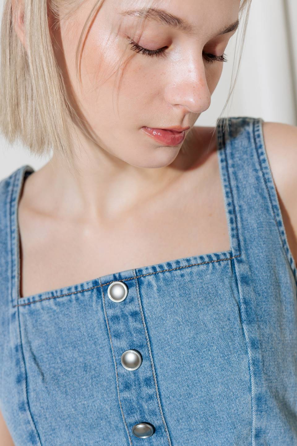 A washed denim top featuring square neckline, sleeveless, front button detail and smocked back with zipper closure.