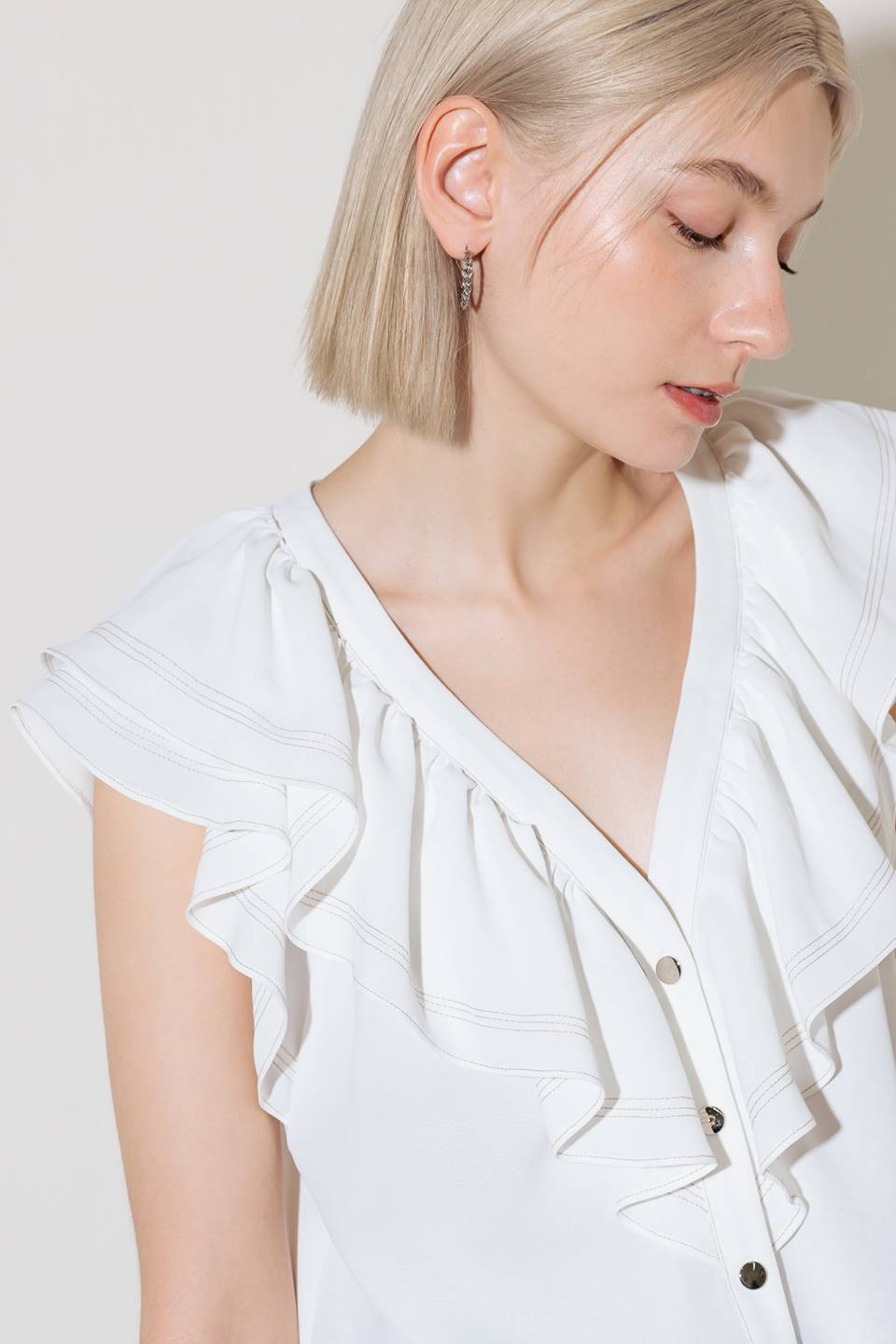 A solid woven top featuring V neckline, ruffles and button down.