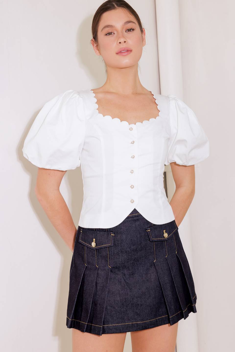 A solid woven top featuring square neckline with scalloped edge, short puff sleeve, front button down and back tie