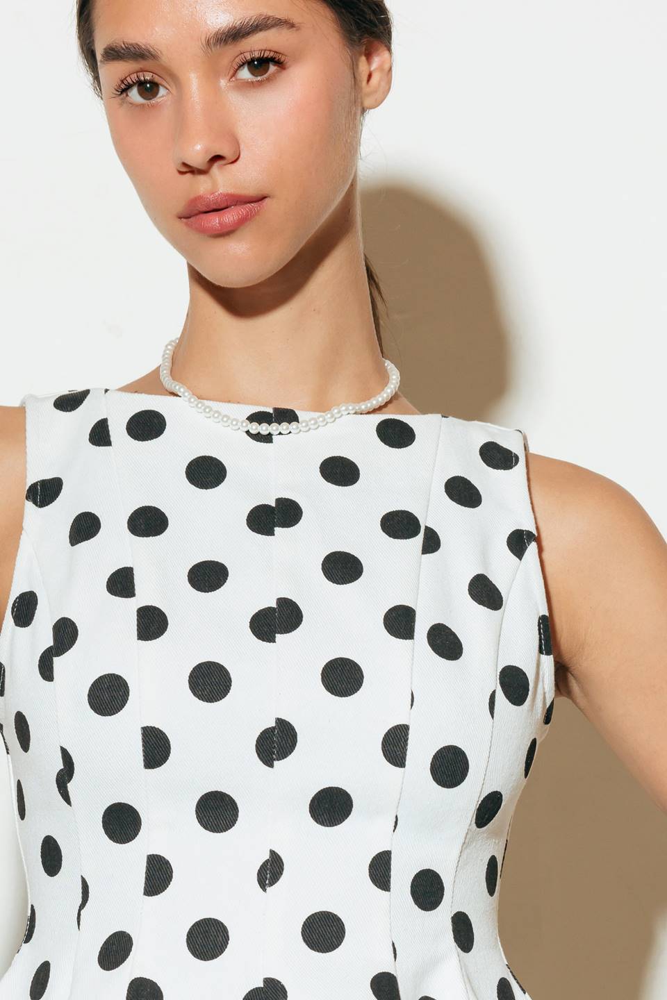 A white, polka-dotted printed woven top featuring wide neckline, peplum, V back and zipper closure.