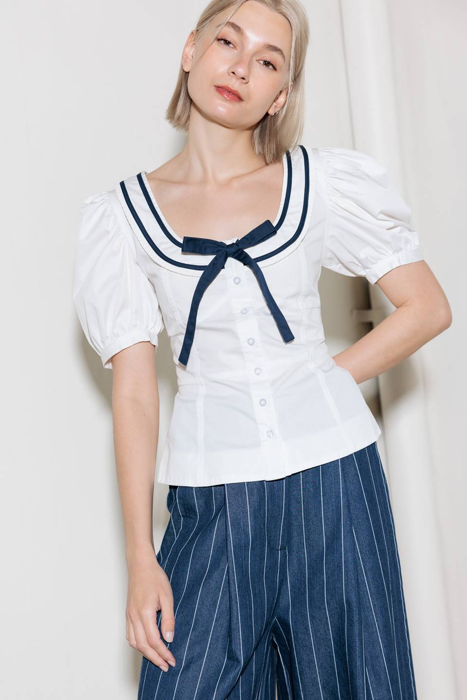 A solid woven top featuring U neckline, front bow, short puff tie and button down.