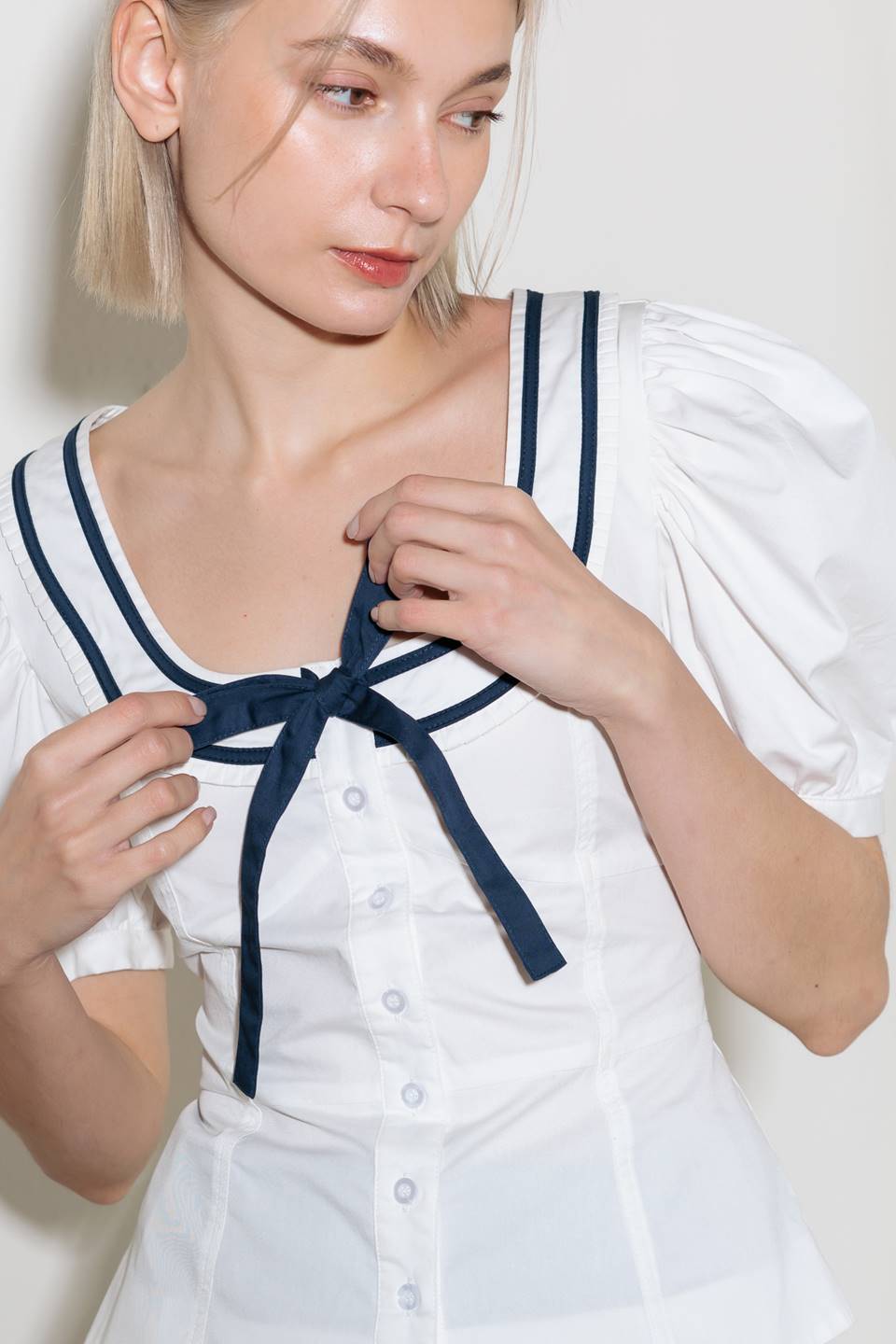 A solid woven top featuring U neckline, front bow, short puff tie and button down.