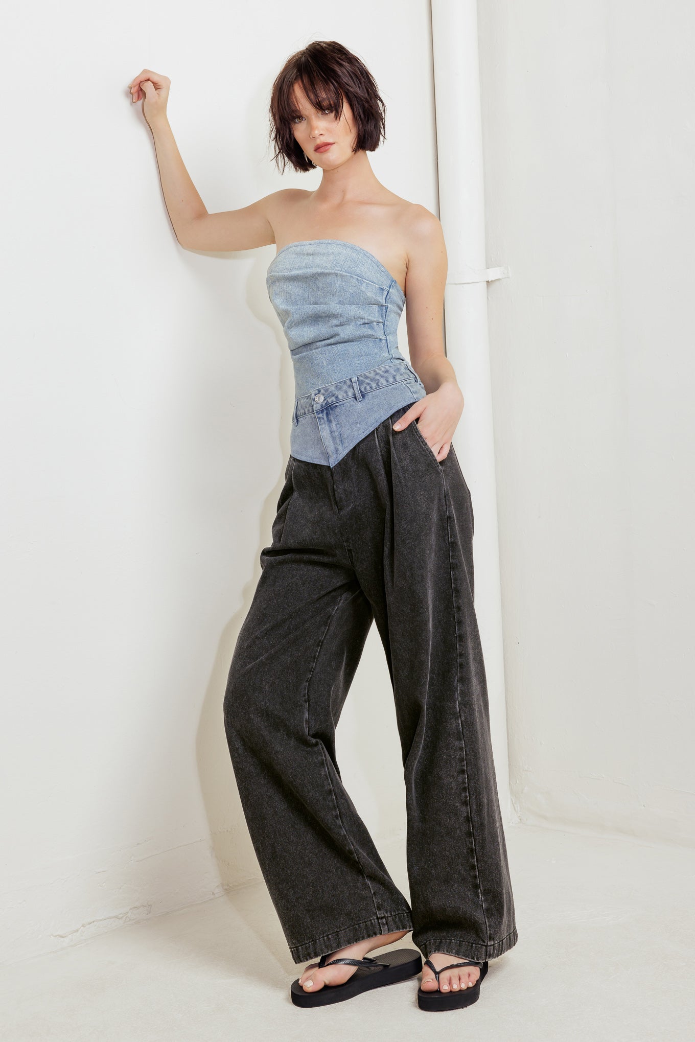 An acid-washed denim bodysuit featuring strapless, side shirring and bottom snap button closure