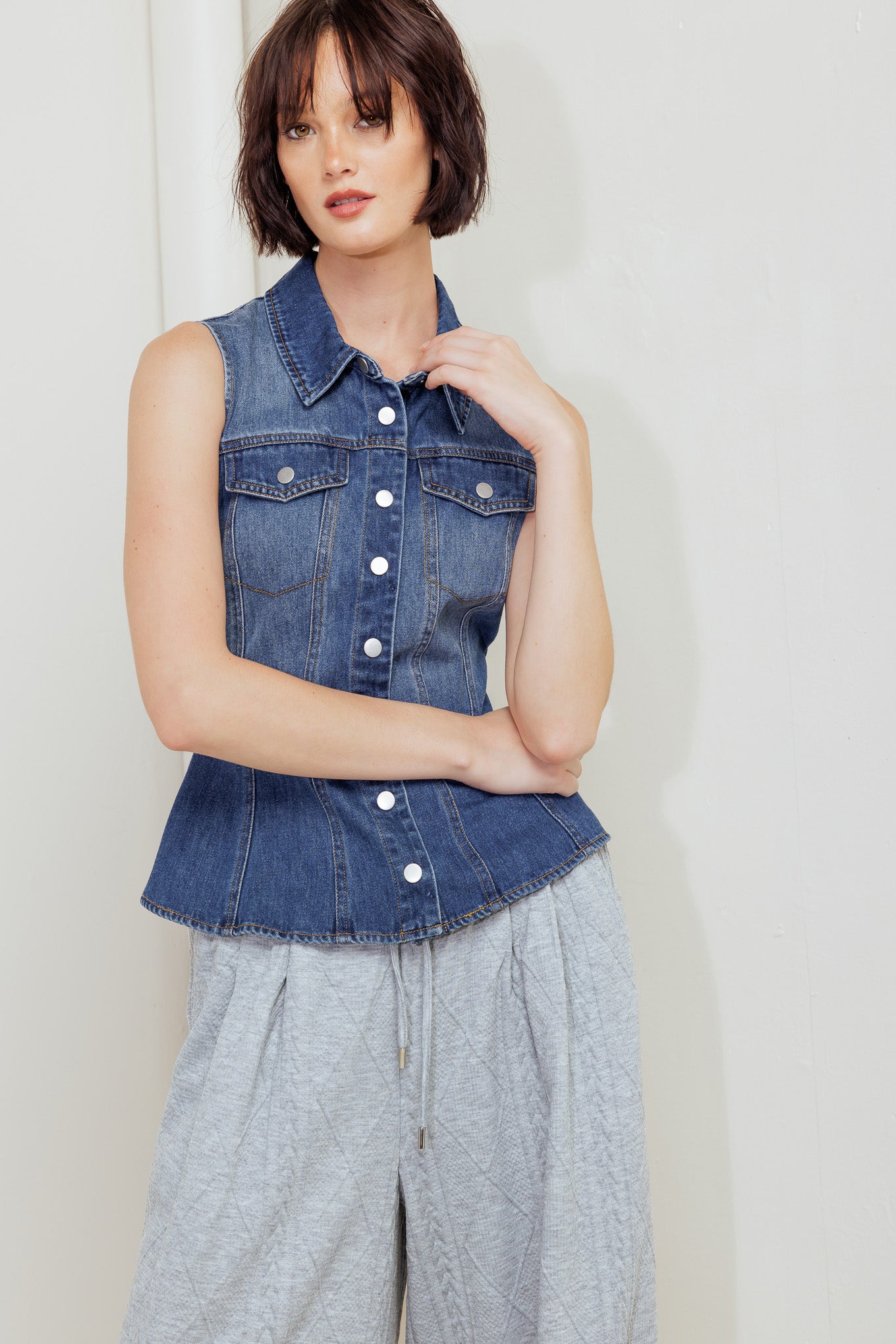 A washed denim top featuring collar, sleeveless, button down, pockets and peplum