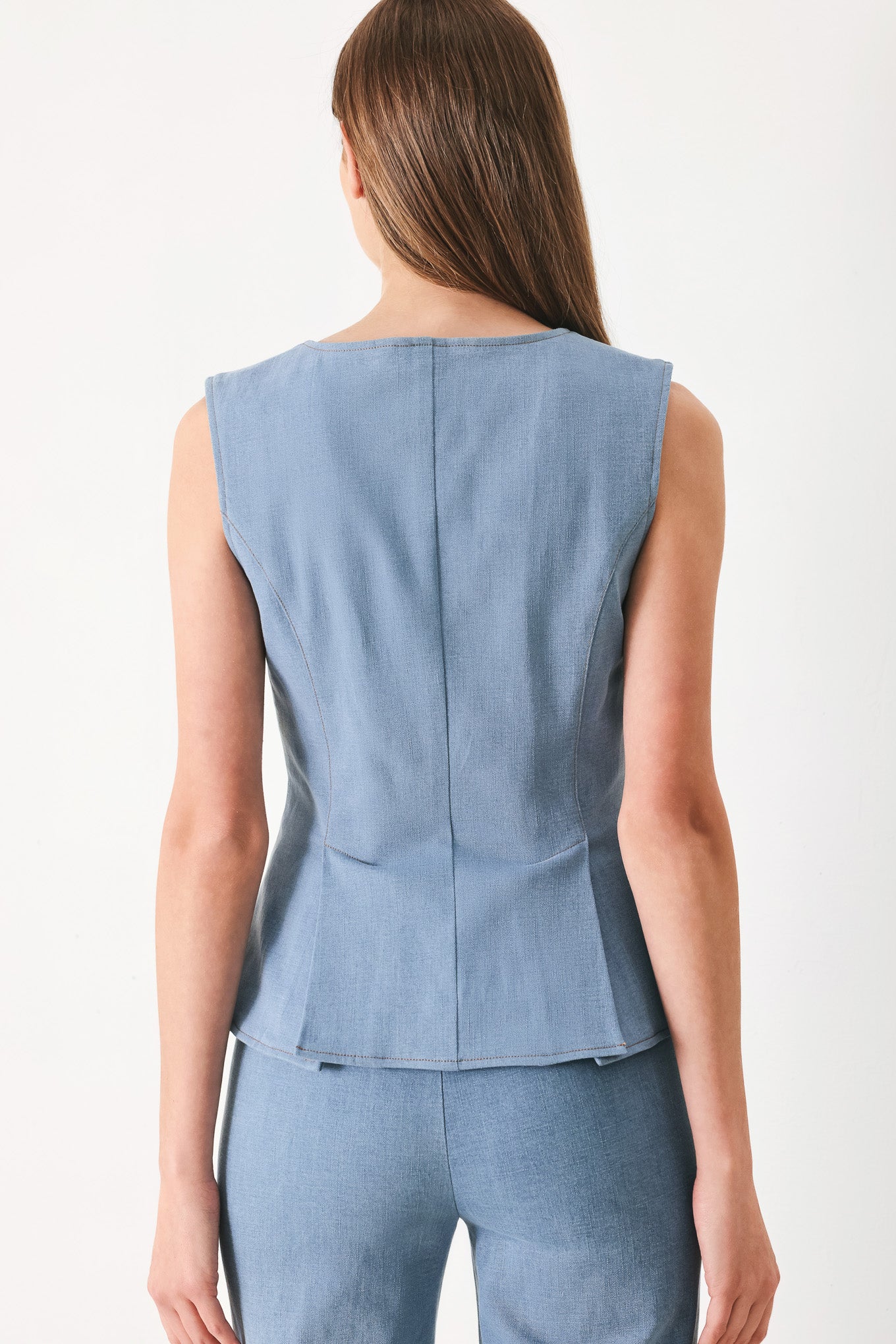 Woman wearing a light blue sleeveless peplum top featuring round neckline and front zipper closure | FREEMARKET | Flying Tomato