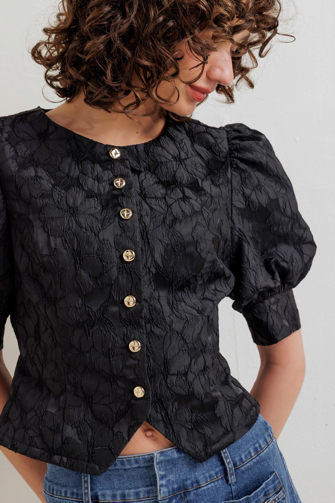 A textured woven top featuring round neckline, short puff sleeve with cuff and front button down closure