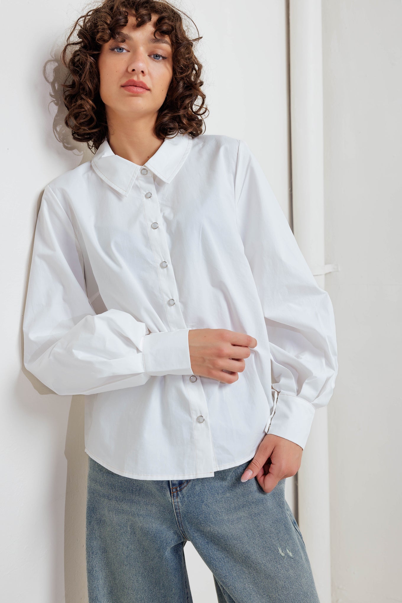 A solid white woven top featuring collar, front snap button down and long sleeve