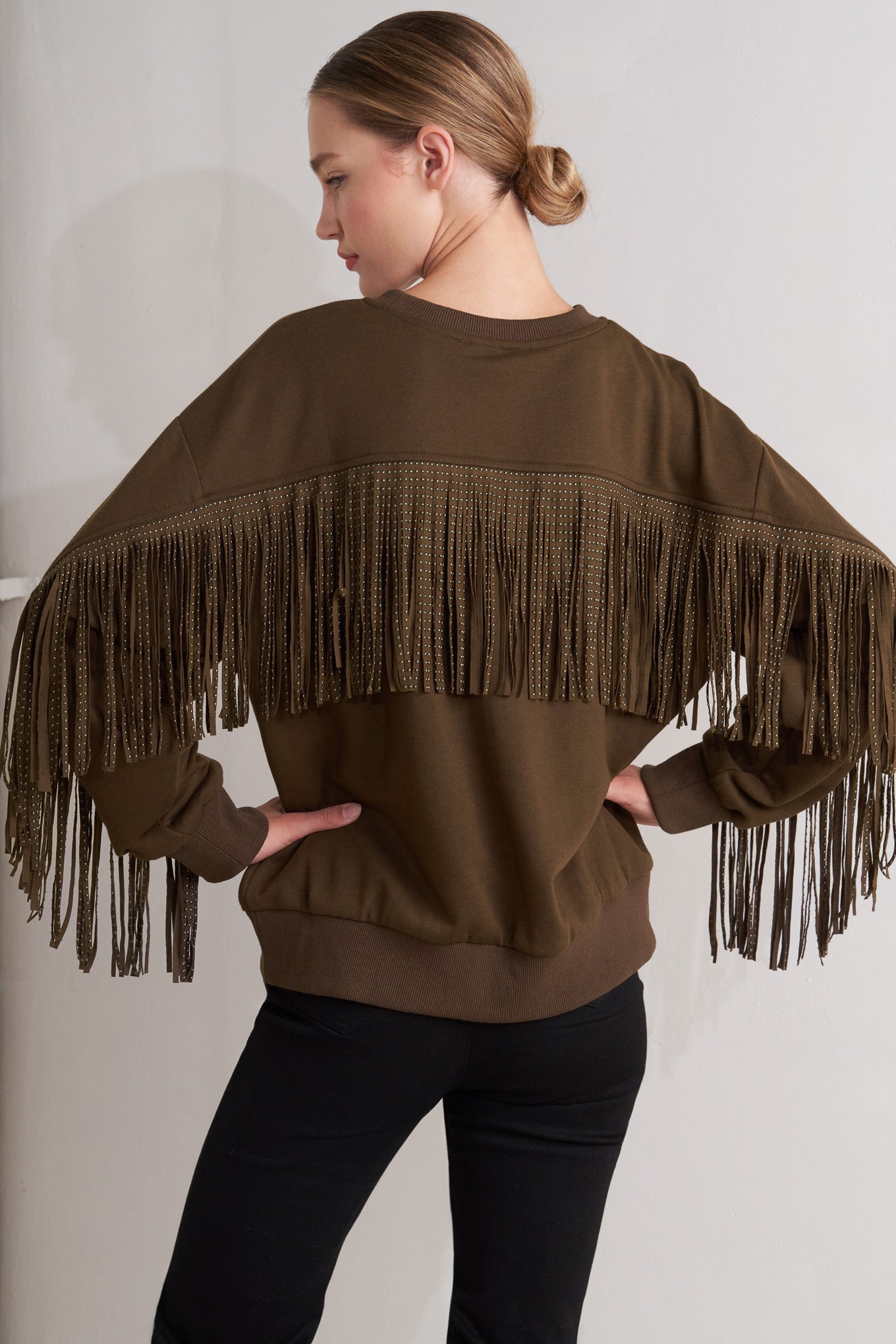 A pullover knit top featuring crew neckline, long sleeve and stud embellished fringe back detail