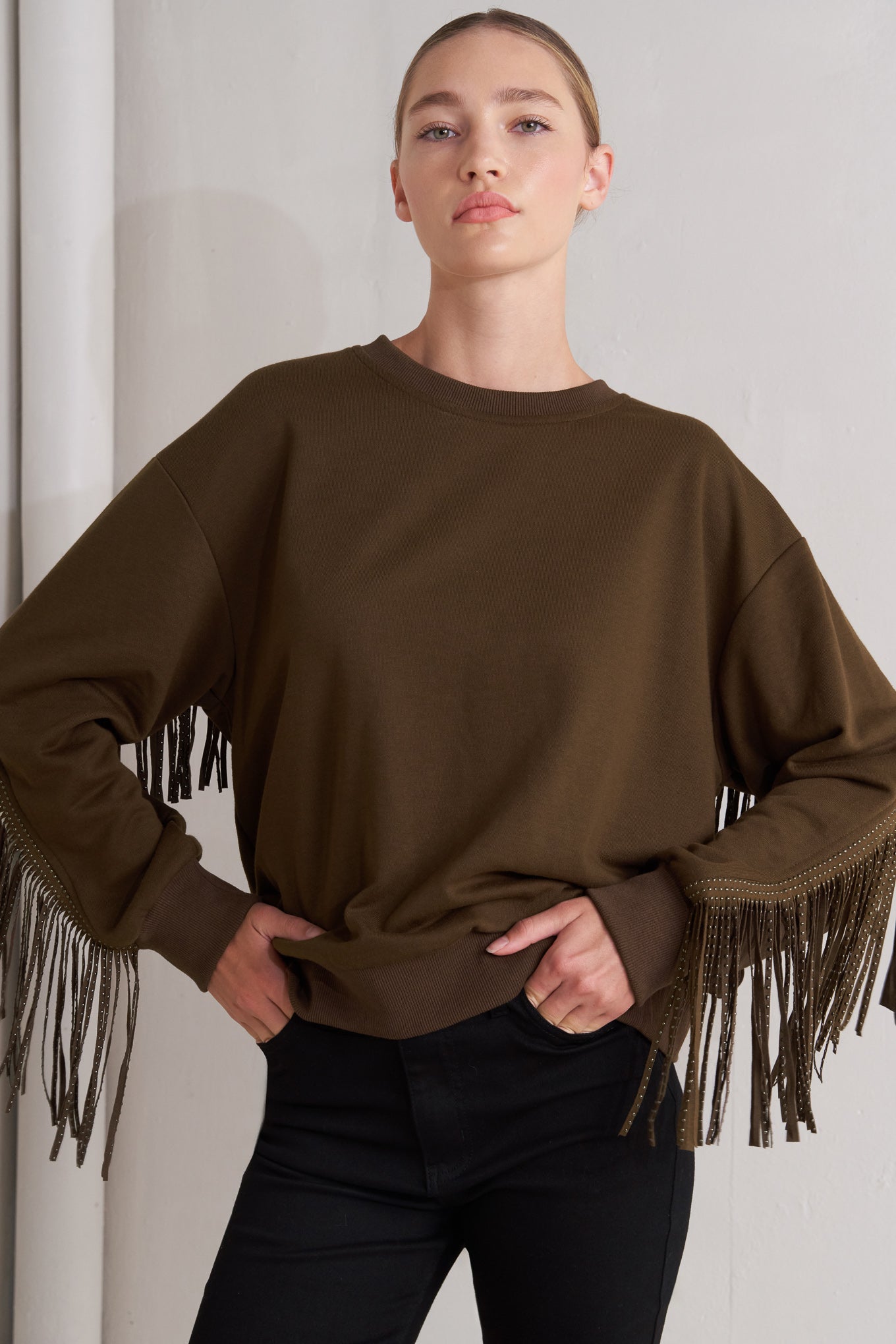 A pullover knit top featuring crew neckline, long sleeve and stud embellished fringe back detail