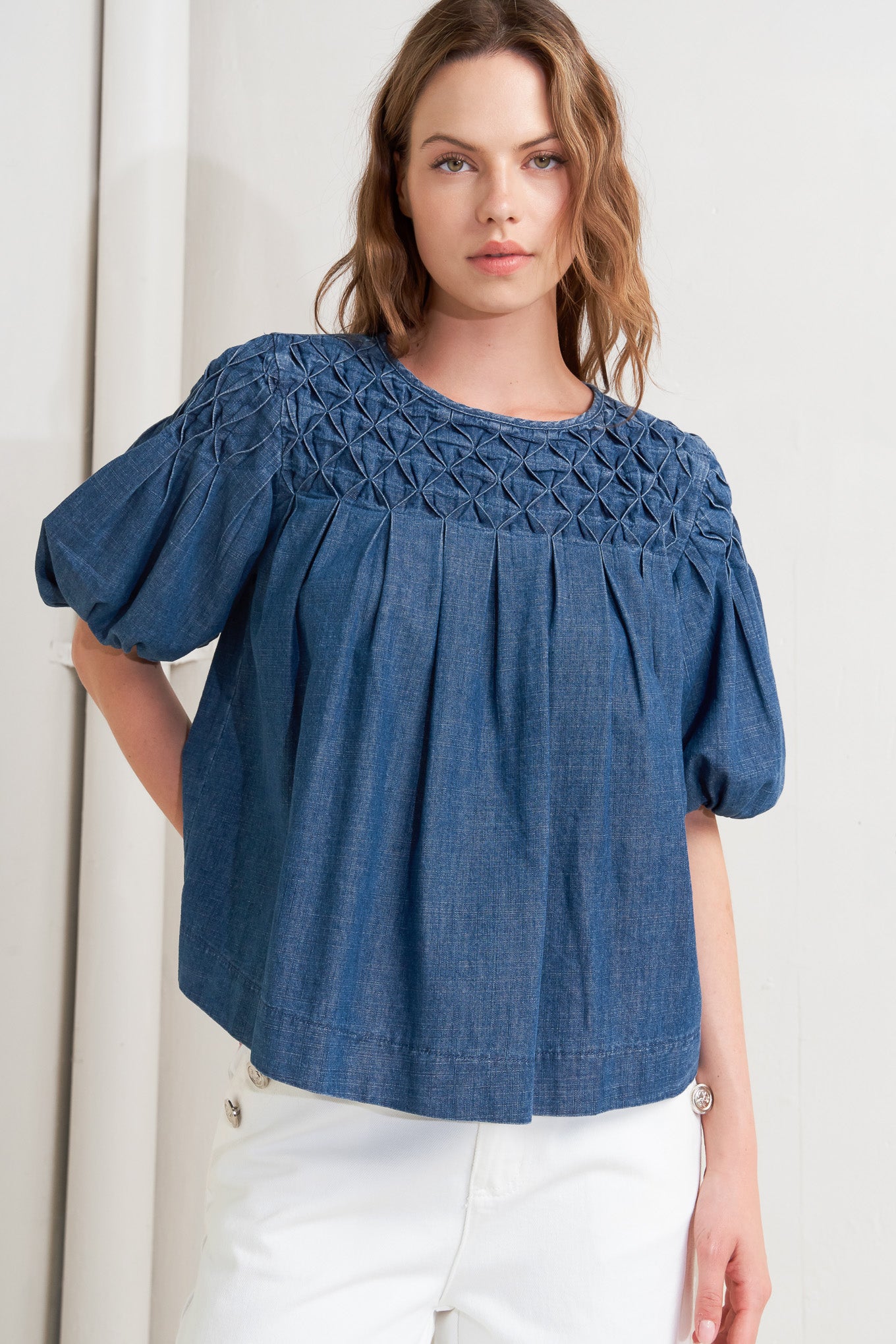 A chambray top featuring round neckline, honeycomb smocked, short bubble sleeve and back button closure