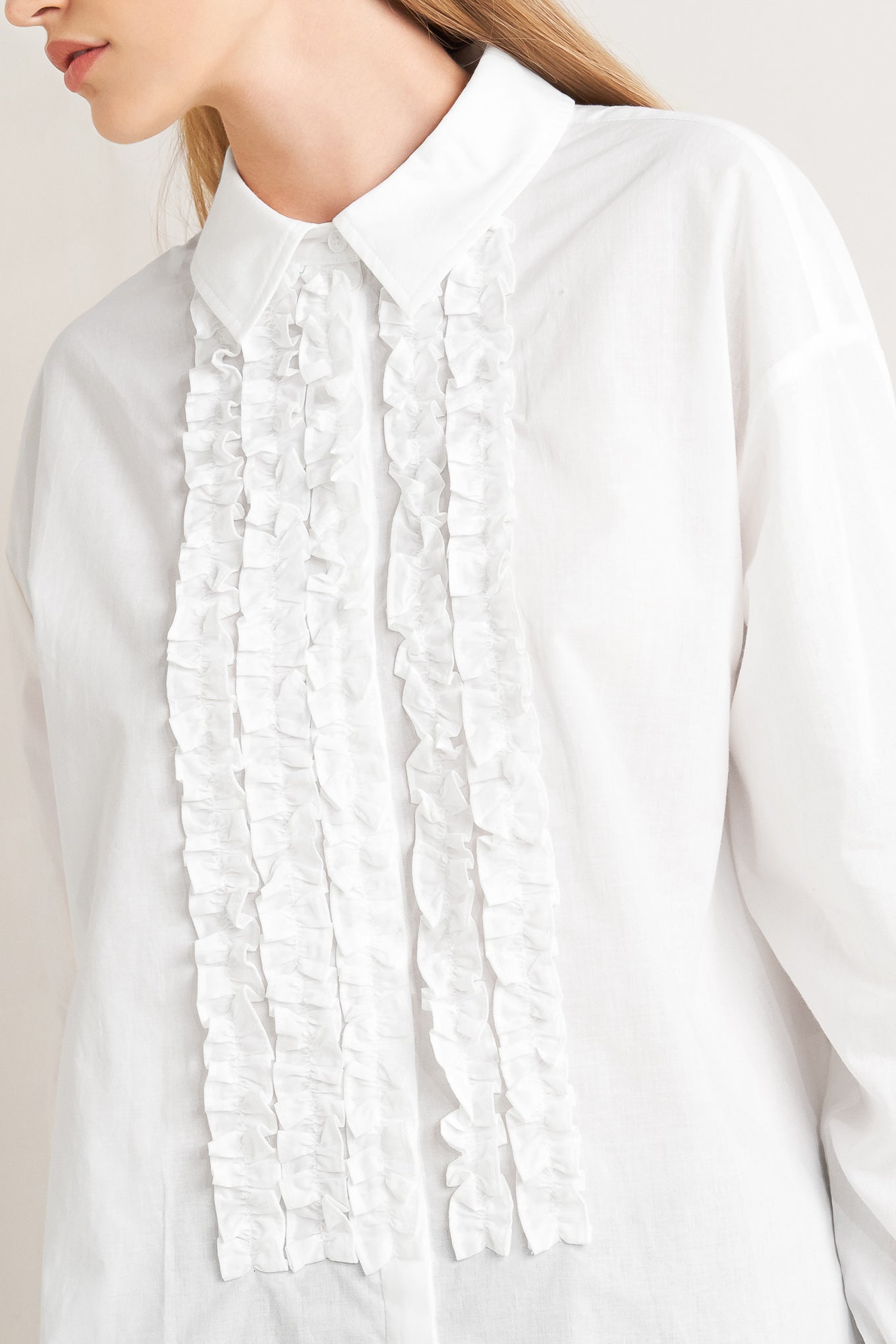 A solid woven top with a collar, button-down front, long sleeves, and front ruffle detail.