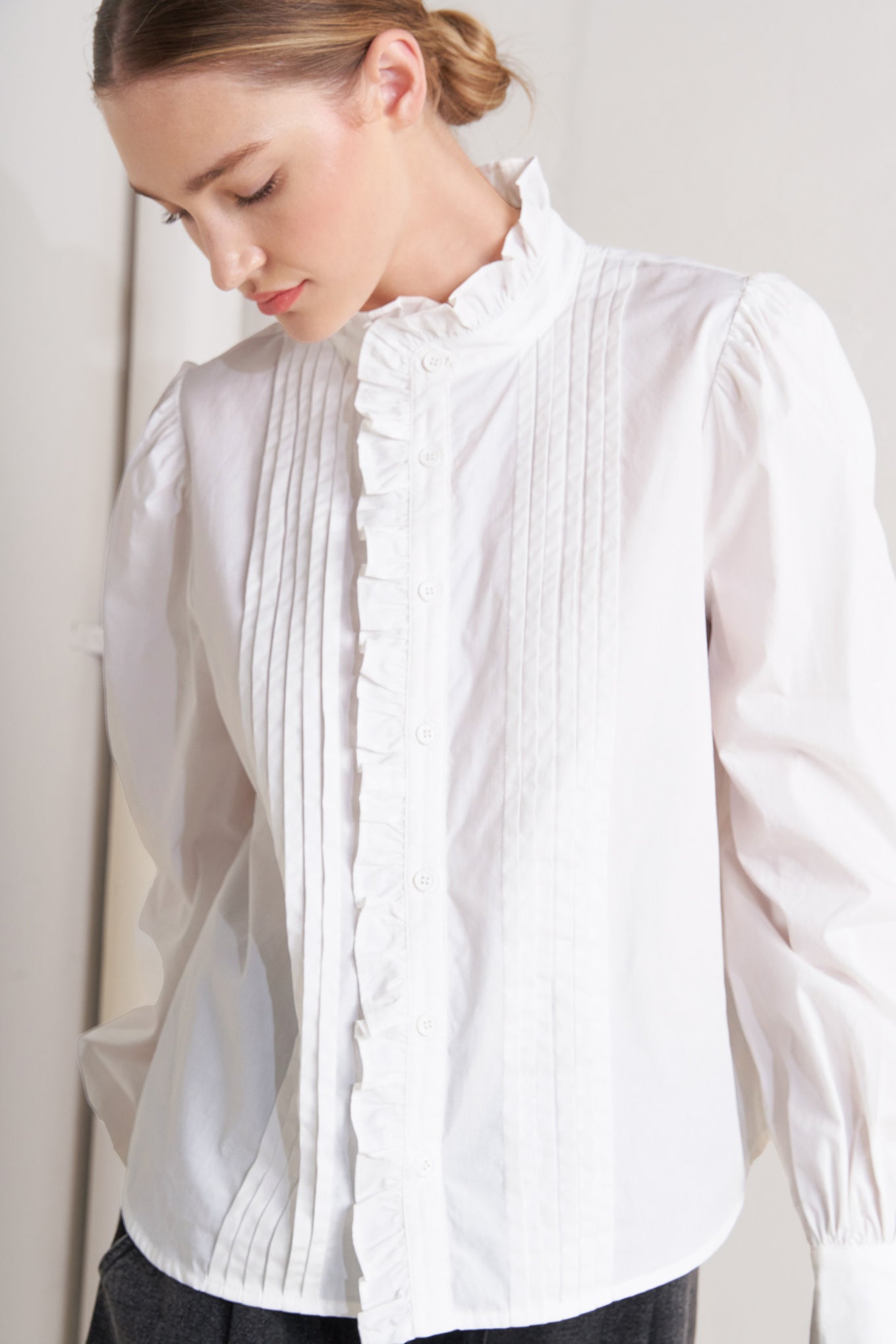 A solid woven top featuring ruffled high neckline, long sleeve and front button down closure