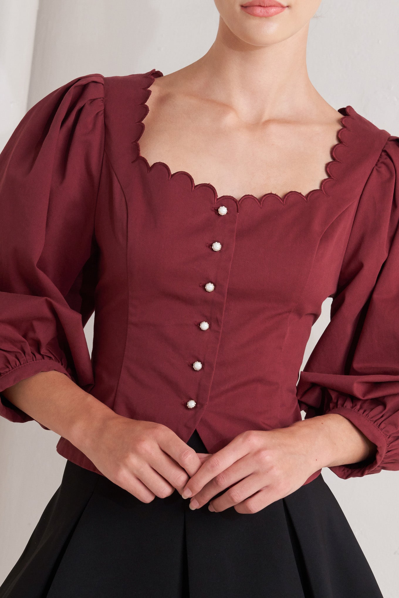 A solid woven top featuring scalloped square neckline, 3/4 sleeve and front button down closure