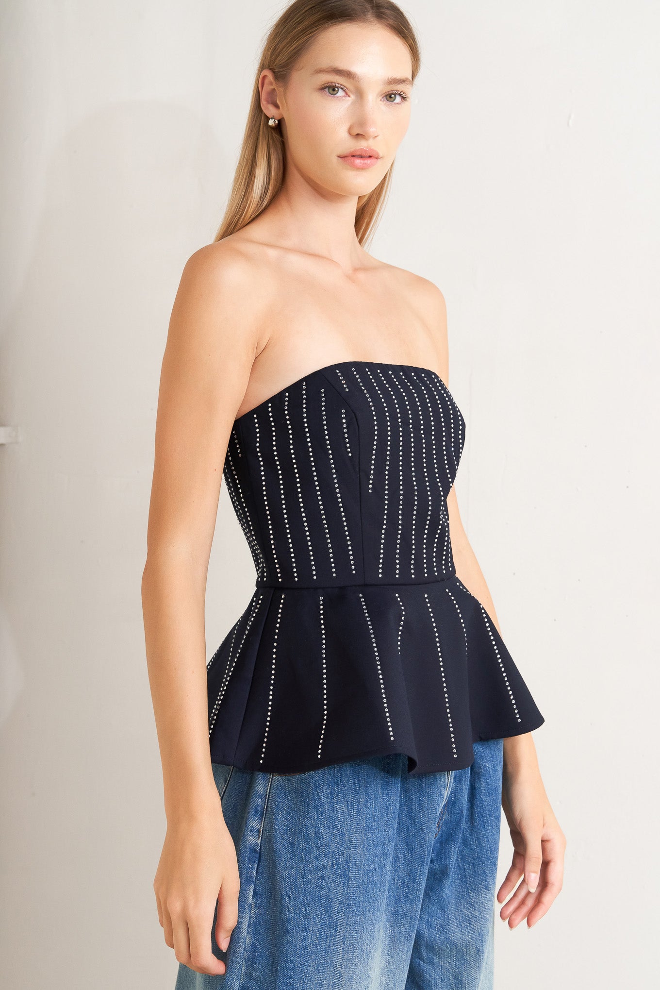 A solid woven top with embellishment, strapless neckline, peplum and back zipper closure