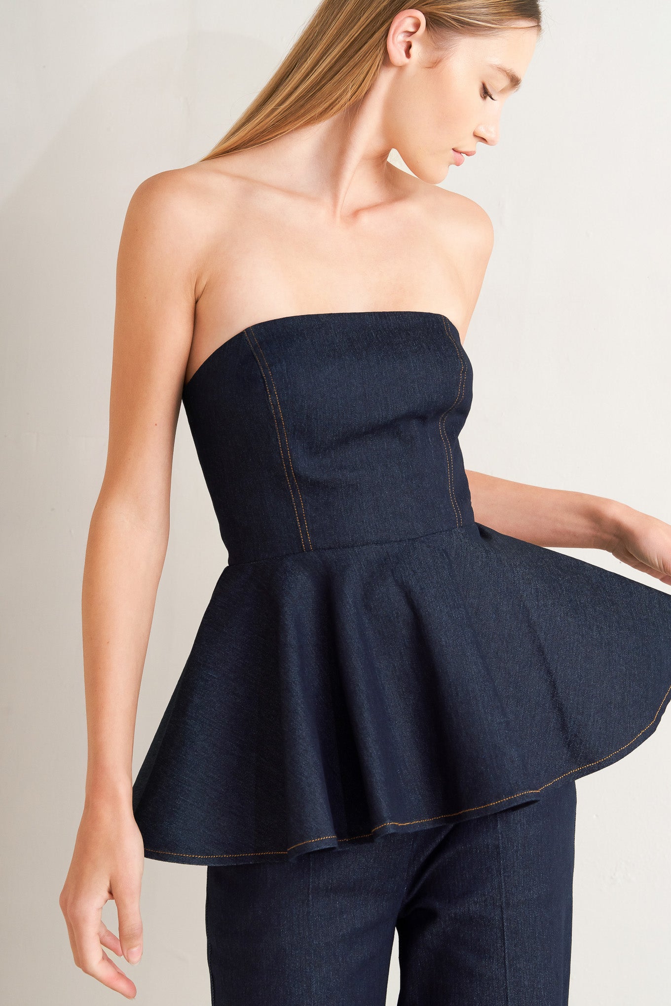 A denim top featuring strapless, peplum and back zipper closure.