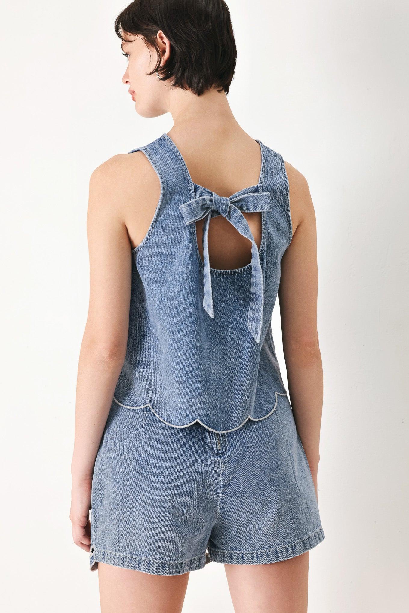 A washed denim top featuring round neckline, sleeveless, eyelet cut out and scallop hem with back tie closure