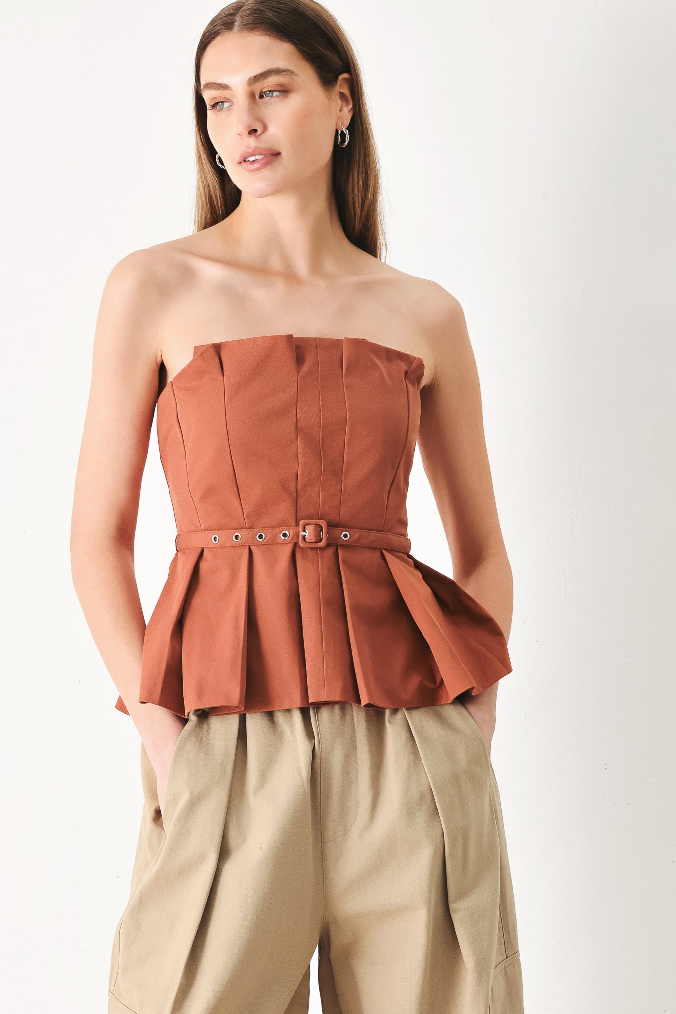 Woman wearing a rust-colored strapless top with a belt featuring knife pleats | Flying Tomato