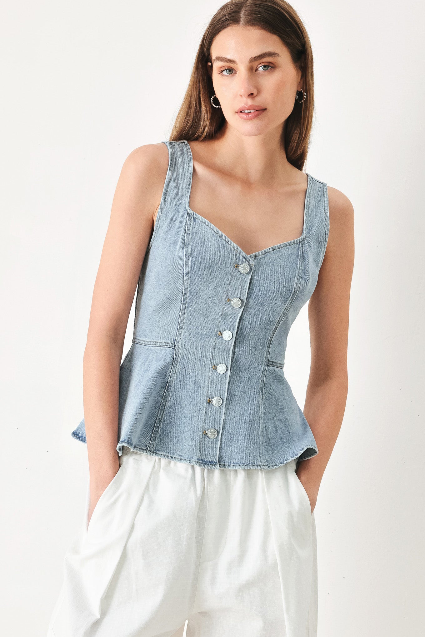 Woman wearing a sleeveless denim peplum top featuring Queen Anne neckline, sleeveless, front button down | FREEMARKET | Flying Tomato