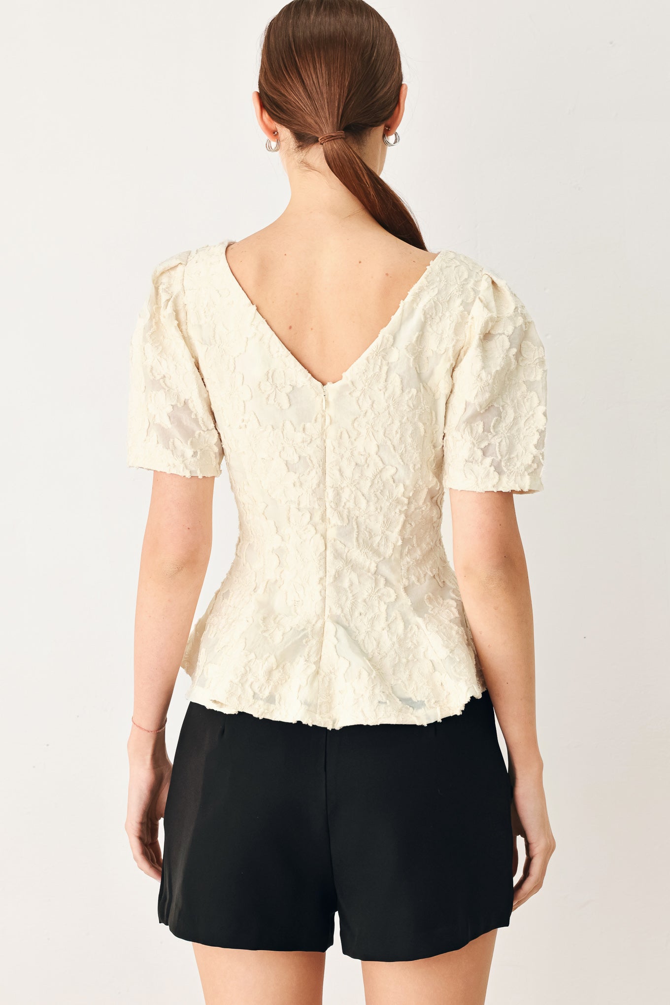 Woman wearing a white lace jacquard top featuring round neckline, short sleeve, peplum and V back with zipper closure | FREEMARKET