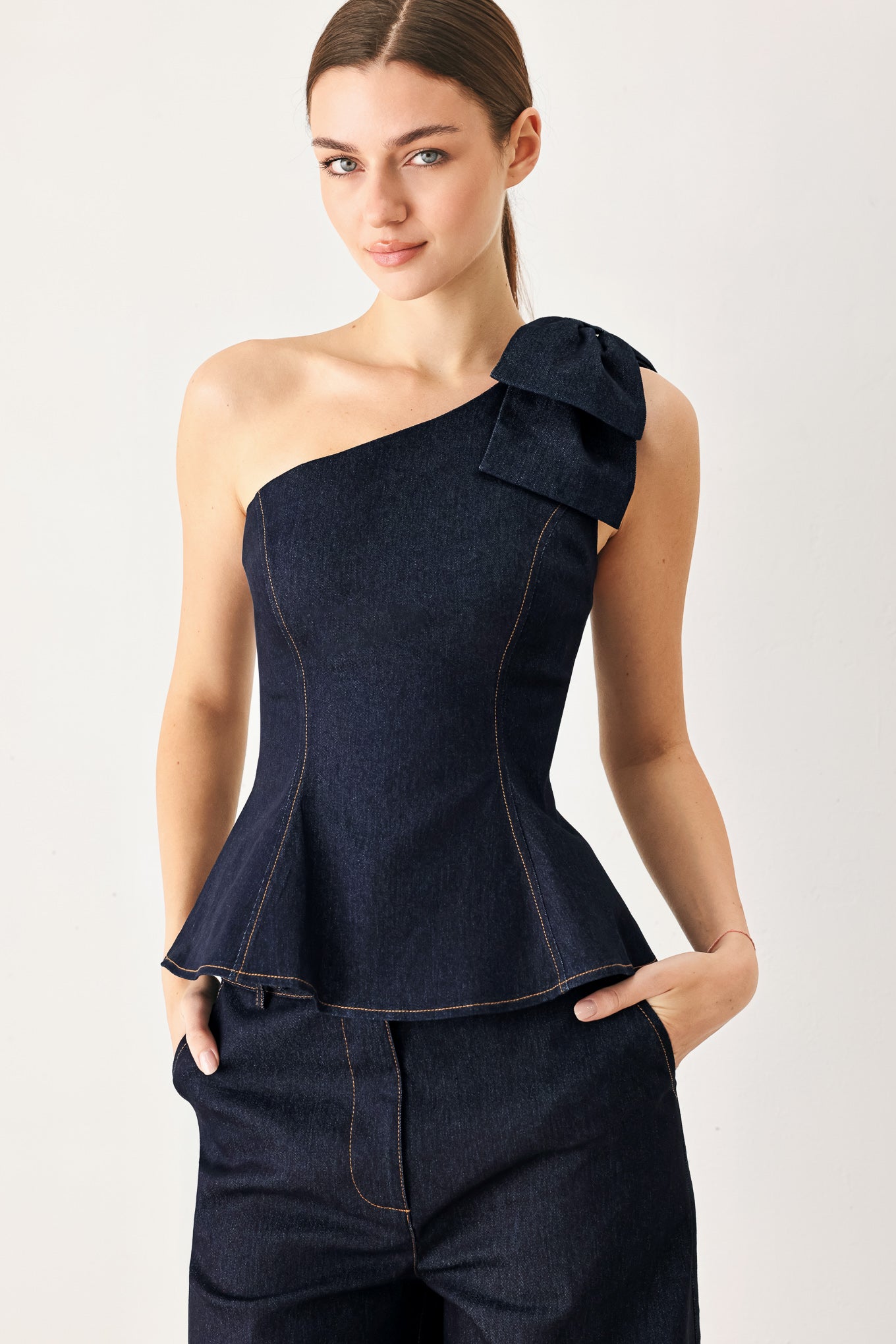 Woman wearing a dark blue denim one-shoulder peplum top with bow detail | Flying Tomato