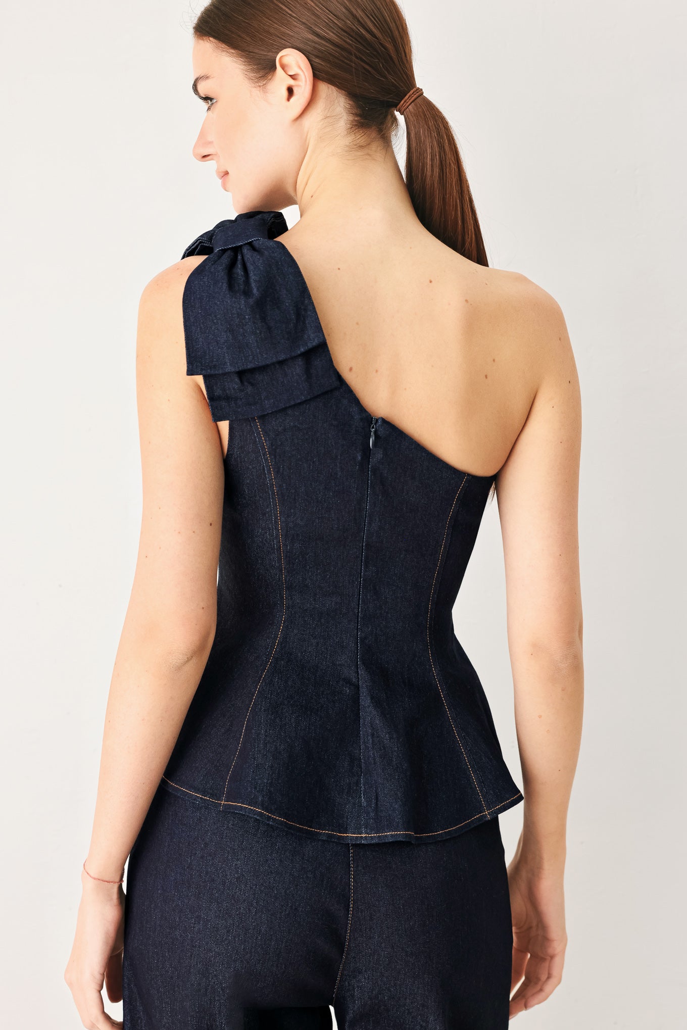 Woman wearing a dark blue denim one-shoulder peplum top with bow detail | Flying Tomato