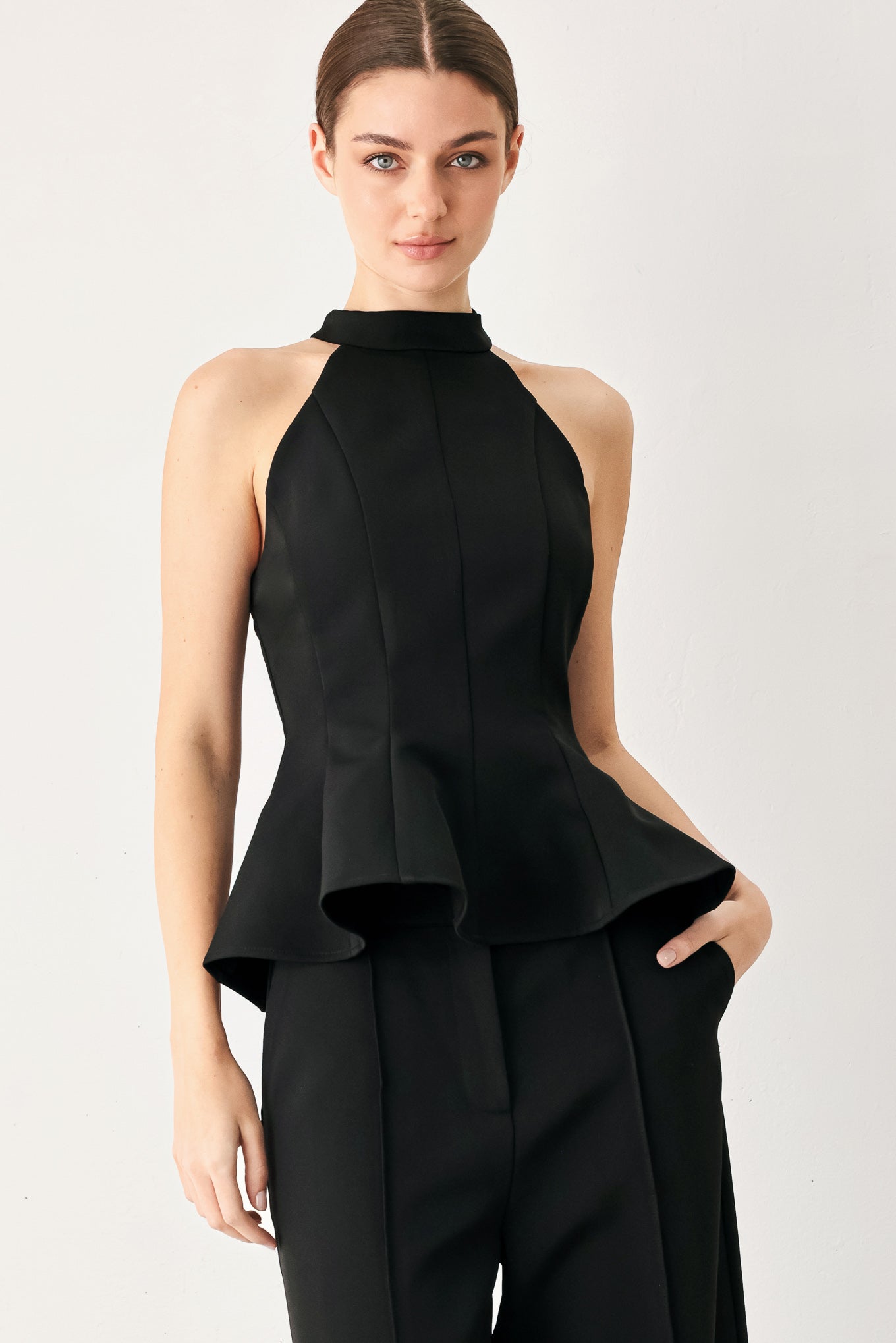 Woman wearing a black solid woven top with halter neckline, peplum and back zipper closure | FREEMARKET