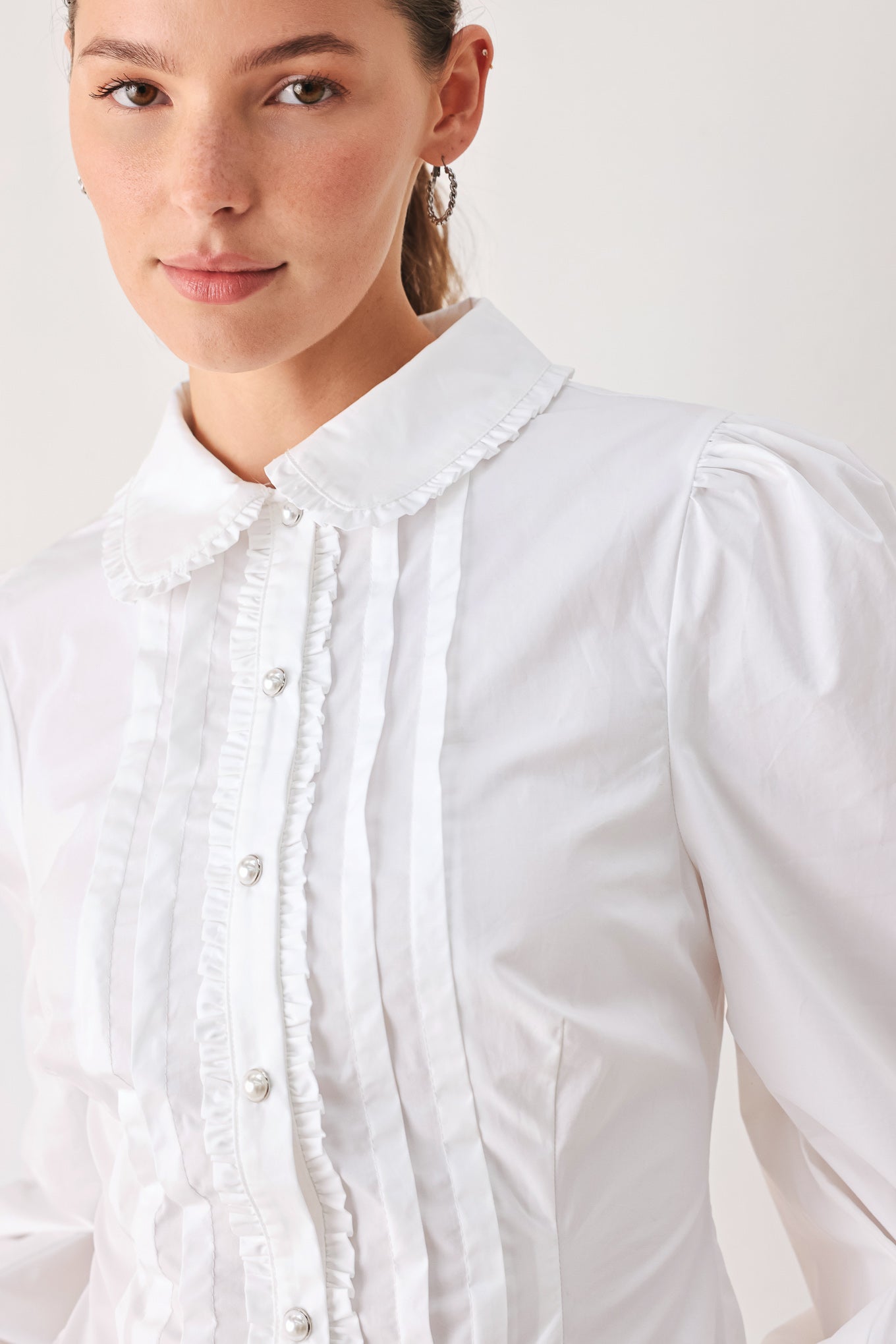 A woman wearing a white long-sleeve blouse with a high collar, decorative front pleats, and puffed shoulders | FREEMARKET