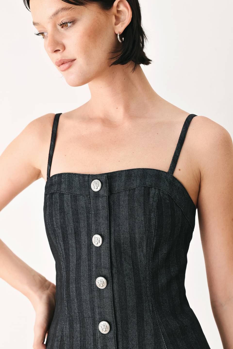 A model wearing a dark gray pinstriped jumpsuit with a structured corset-style bodice, thin shoulder straps, and prominent silver-tone decorative buttons down the front and on the waist | FREEMARKET