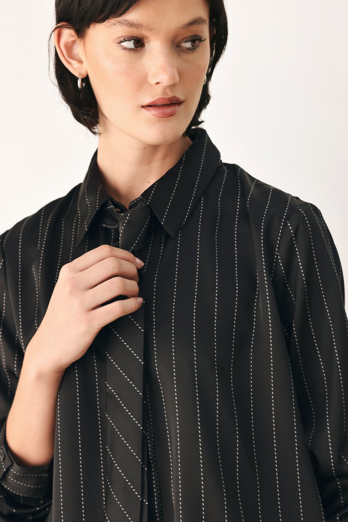 A woman wearing a black long-sleeve button-up shirt with thin white vertical pinstripes, styled with a matching striped tie | FREEMARKET