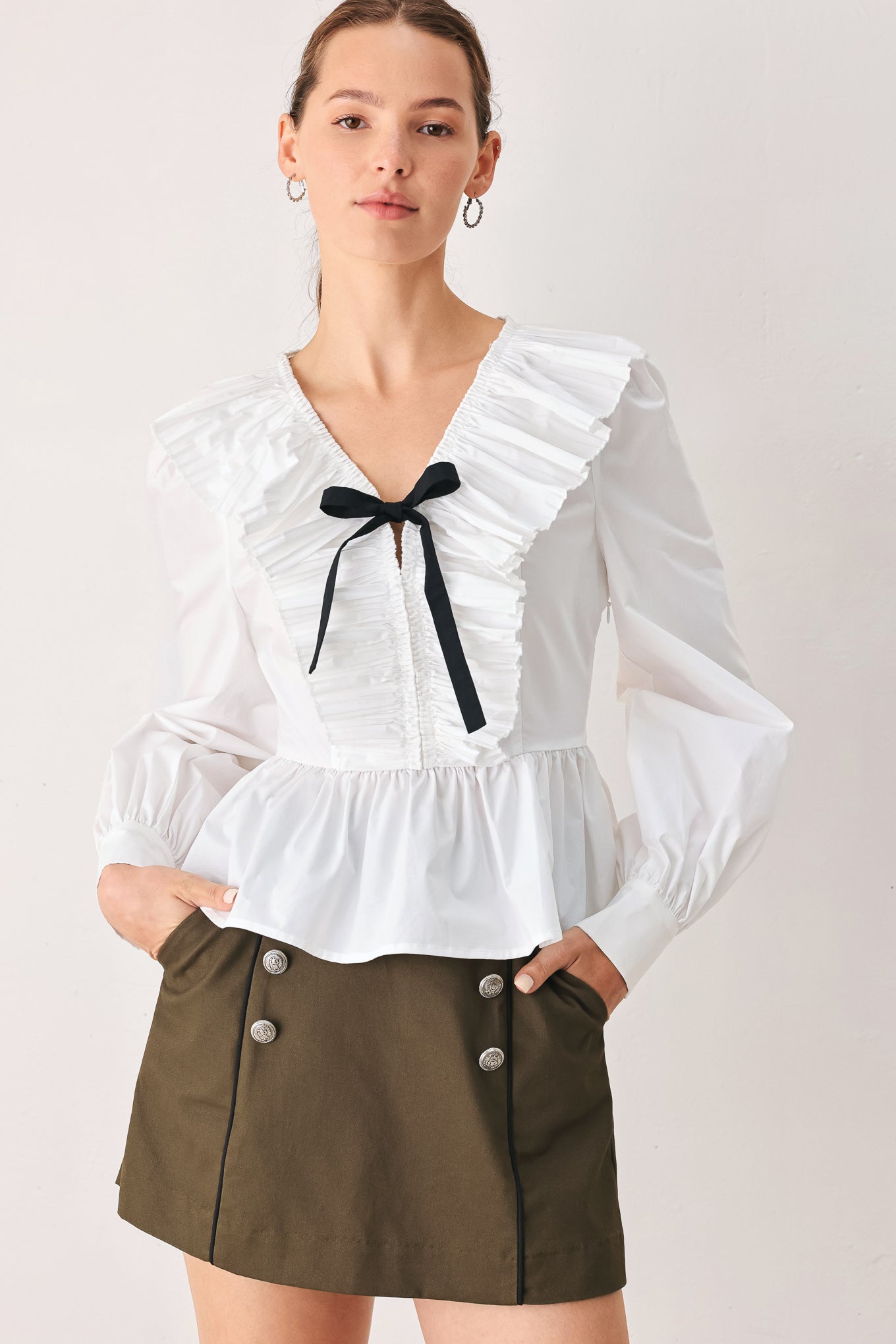 A woman wearing a white long-sleeve blouse with a ruffled V-neck, gathered waist, and a black ribbon bow at the center | FREEMARKET