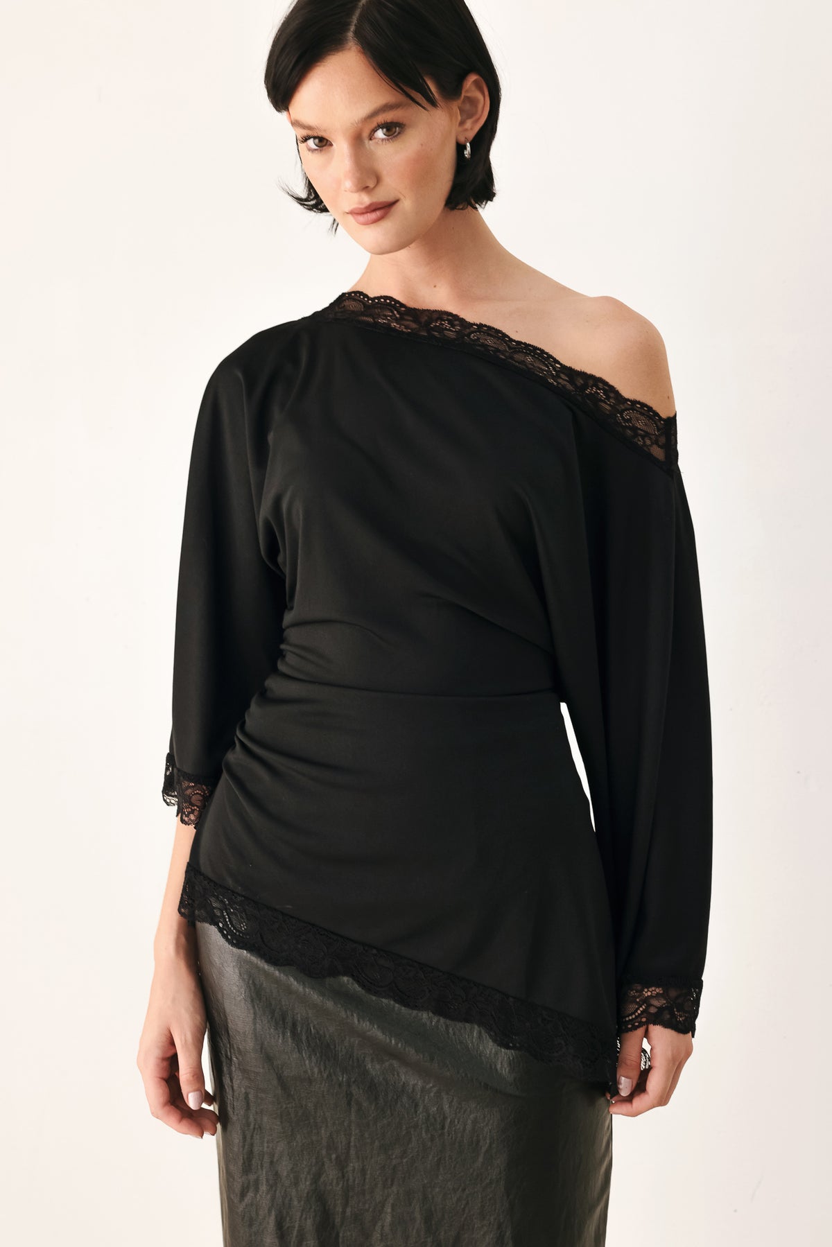 A model wearing a black asymmetrical off-the-shoulder top with black lace trim along the neckline, cuffs, and hem | FREEMARKET